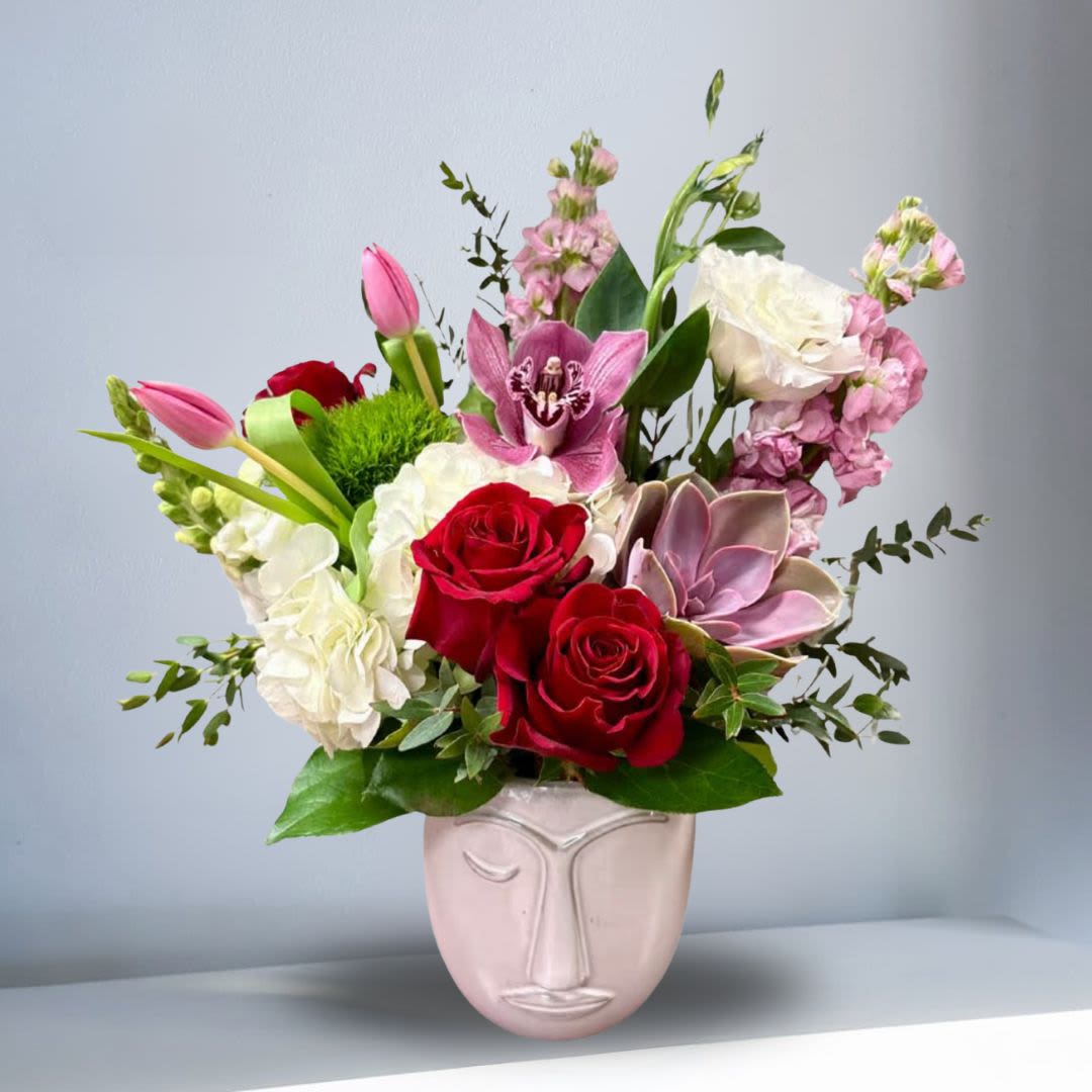 Artistic Kindred Spirit - Art meets nature in this abstract face vase filled with colorful, lively blooms. A stylish way to honor sisterhood, inspire joy, and add a pop of creativity to any space.  Recipe: White Lisianthus, White Snapdragons, White Hydrangea, Red Roses, Pink Tulips, Cymbidium Orchid, Snapdragon, Dianthus barbatus, Pink Stock, and Succulent in beige, abstract face vase. Seasonal: All year round Orientation: Front Facing View Photo shown: Standard