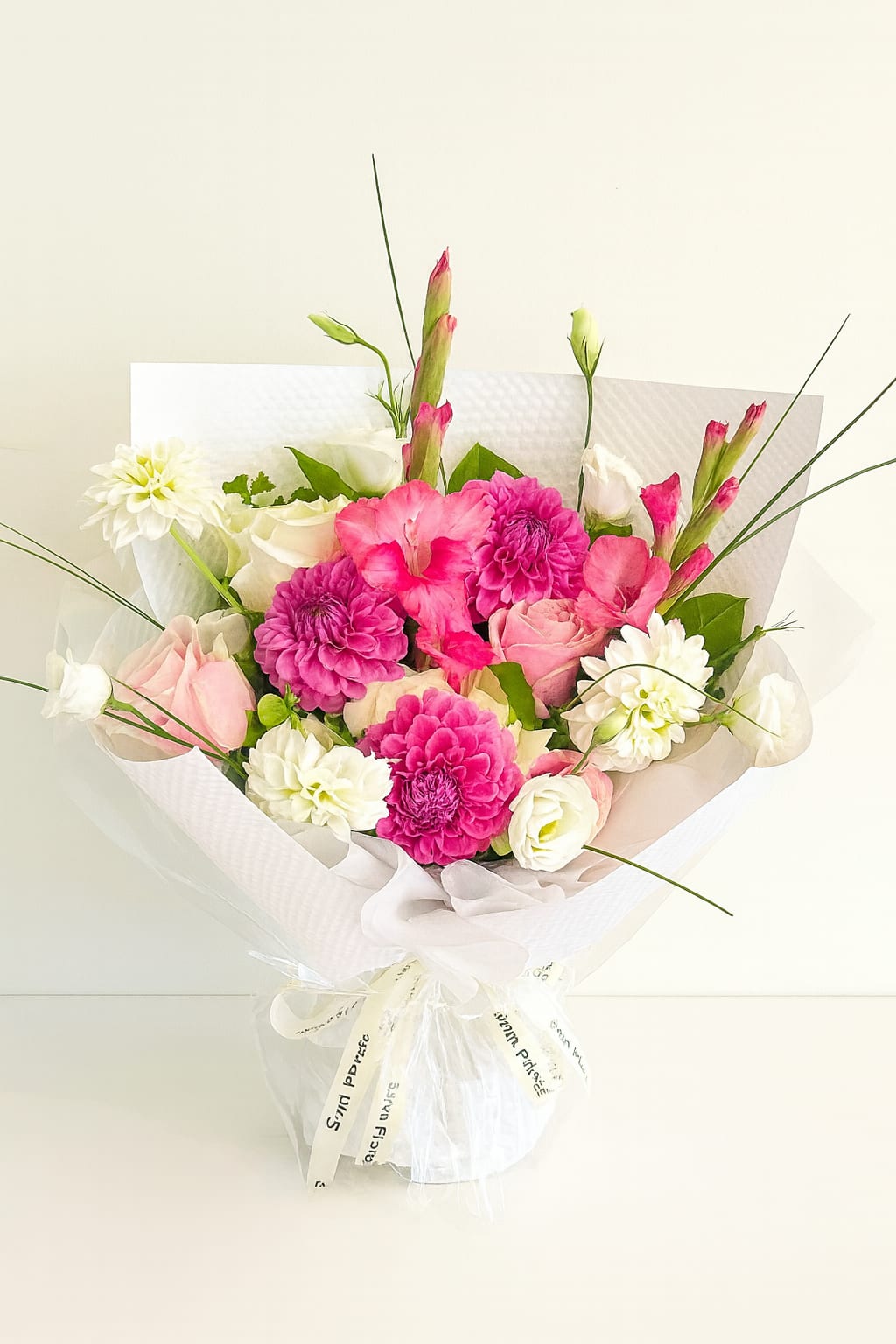 Fuchsia Delight Fuchsia Delight - Bright, graceful, and full of charm, this hand-tied bouquet combines the beauty of fresh pink dahlias, gladiolus, and roses with creamy white blooms for a perfectly balanced look. Accented with lush greenery and delicate lisianthus, it’s wrapped in crisp white paper and finished with a soft bow—making it an ideal gift for birthdays, celebrations, or simply to bring joy to someone’s day. A statement of elegance and cheer, this bouquet is sure to light up any room with its vibrant pink tones and soft white accents. Perfect for: Birthdays • Anniversaries • Thank You gifts • Everyday elegance