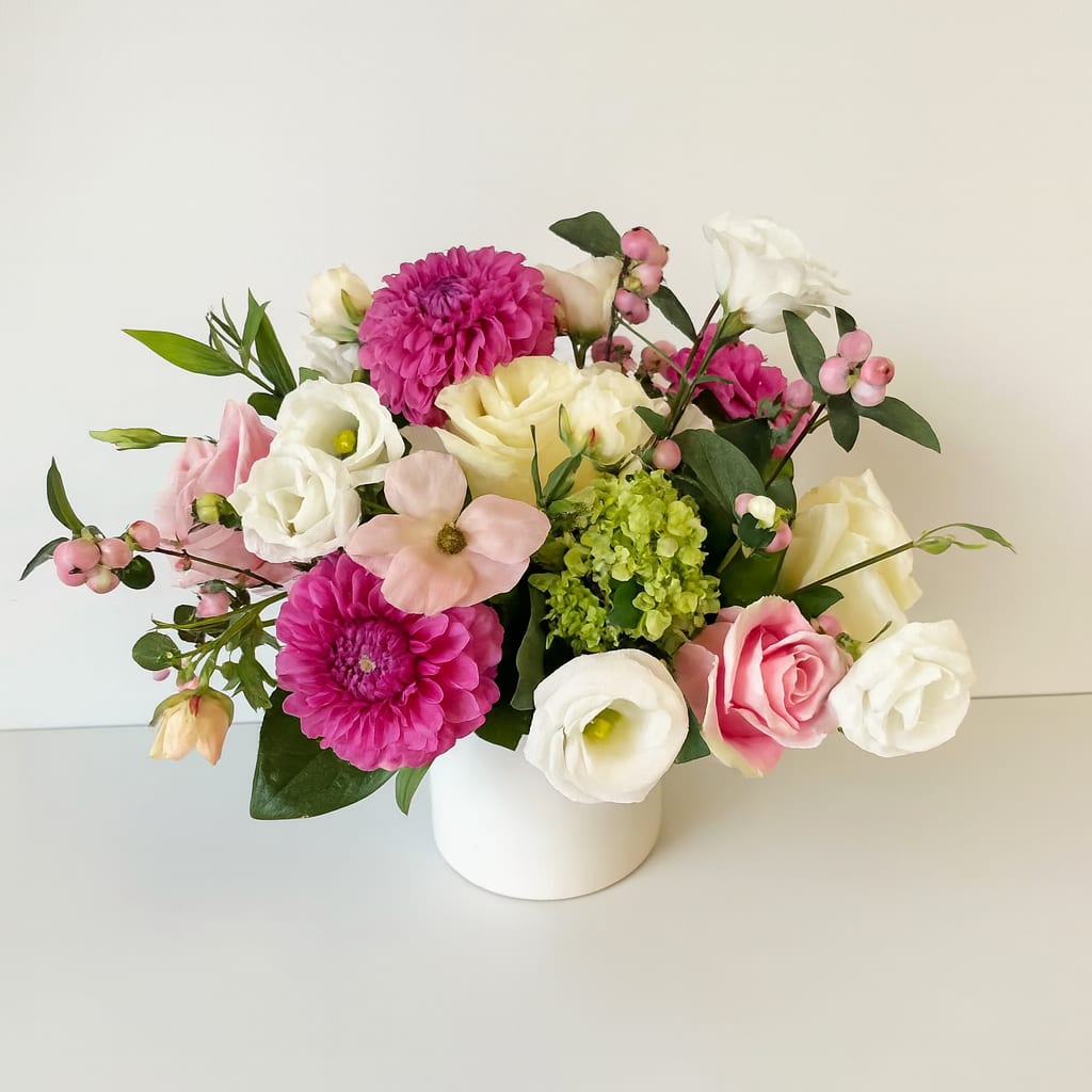 Blush &amp; Fuchsia Charm - A graceful blend of elegance and vibrancy, this arrangement brings together the best of classic and contemporary blooms. Featuring rich fuchsia dahlias, soft blush and ivory roses, delicate lisianthus, and playful pink snowberries, it creates a lush garden-inspired look. A touch of green hydrangea adds freshness, while the clean white ceramic vase enhances its modern appeal.  Perfect for brightening a dining table, adding sophistication to a desk, or gifting a loved one, Blush &amp; Fuchsia Charm is a statement of beauty and joy in every petal.