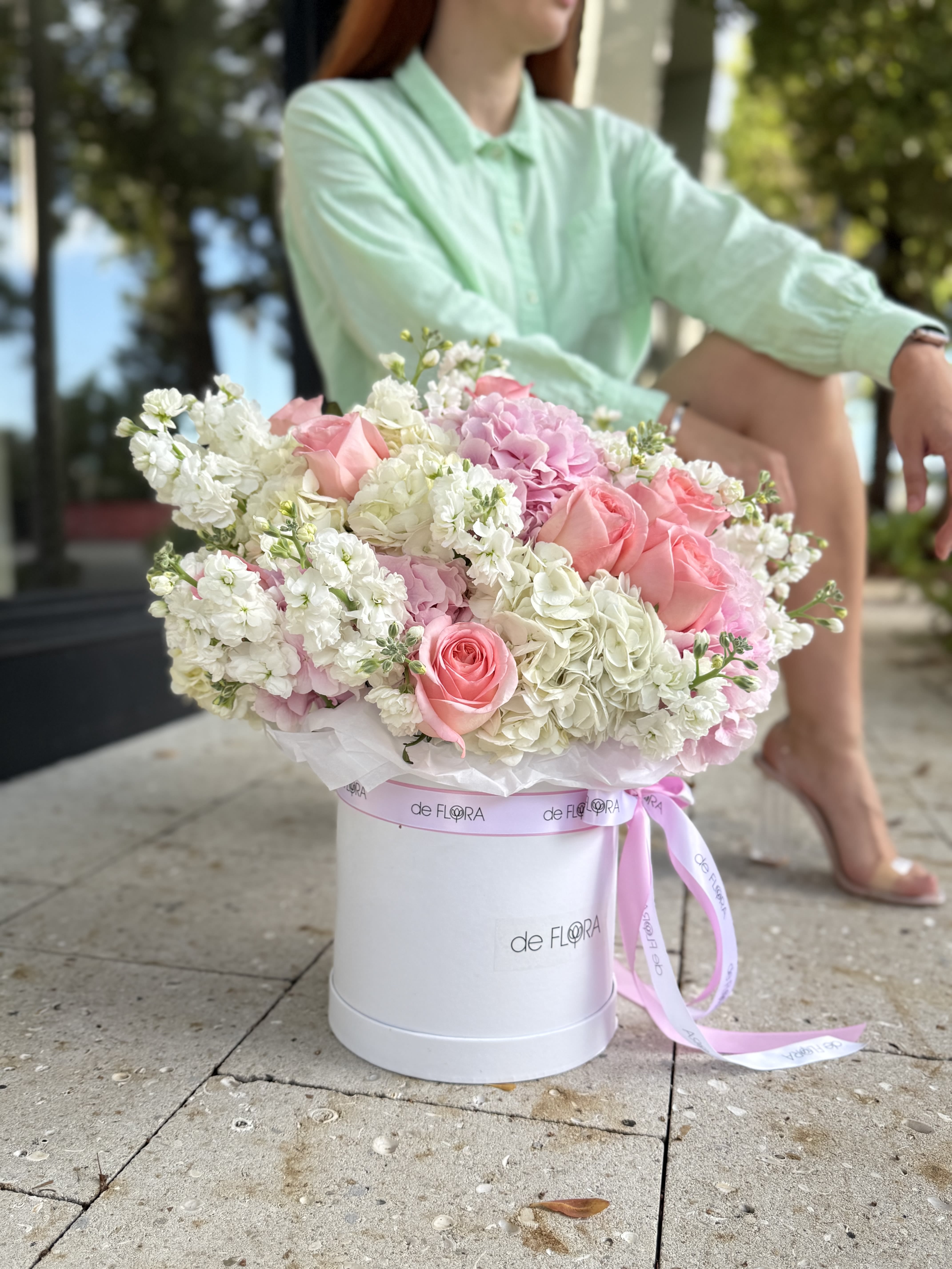 Sugar Cloud - A graceful harmony of pastel blooms, this flower box brings together delicate pink roses, soft hydrangeas, and lush white stock flowers, creating a cloud-like arrangement that radiates romance and refinement. Presented in DeFLORA’s signature round white hatbox, tied with a satin pink ribbon, it is the perfect gift to express tenderness, admiration, and timeless elegance.