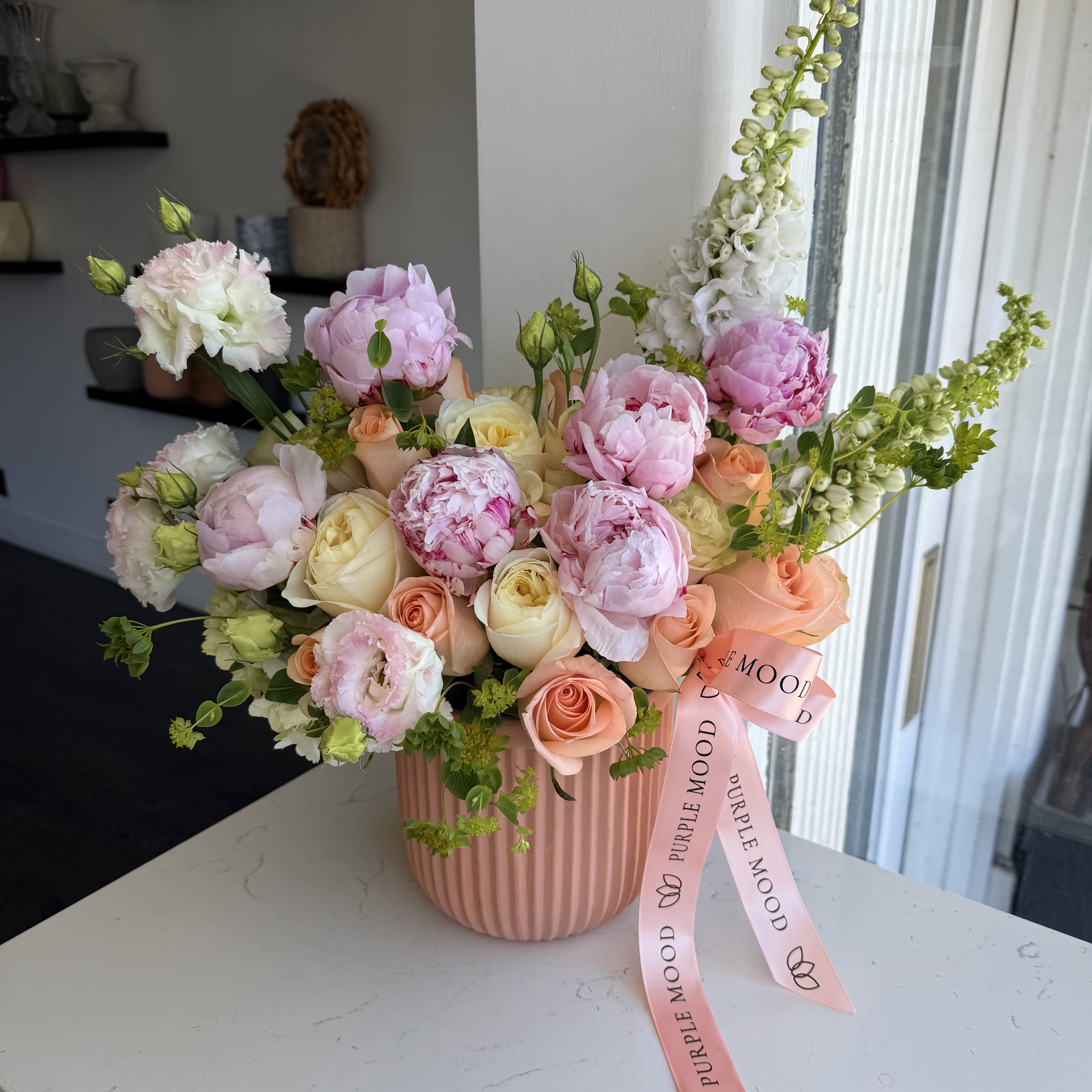 Early Bird Vase Early Bird Vase - The Early Bird Vase is a cheerful and refreshing floral arrangement that radiates the charm of a spring morning. Featuring delicate pink peonies, soft peach and cream roses, and touches of fresh greenery, this design is perfect for bringing light and joy to any space. Arranged in a pastel pink striped vase, it makes an elegant and uplifting gift. • Premium pink peonies, peach roses, cream roses, and seasonal greens • Presented in a stylish pastel pink striped vase • Available in Standard ($219) and Deluxe ($395) sizes • Ideal for birthdays, spring celebrations, or simply brightening someone’s day