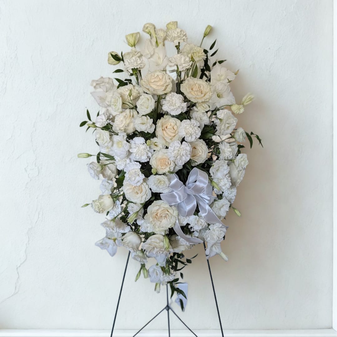 Eternal Grace Standing Spray - A serene and white elegant standing spray, designed with an abundance of pristine white blooms to convey peace, reverence, and heartfelt sympathy. Featuring lush roses, delicate lisianthus, and classic carnations, accented with fresh greenery and a satin ribbon, this arrangement offers a beautiful tribute to honor and remember a cherished life. Perfect for expressing condolences and bringing comfort during times of loss.