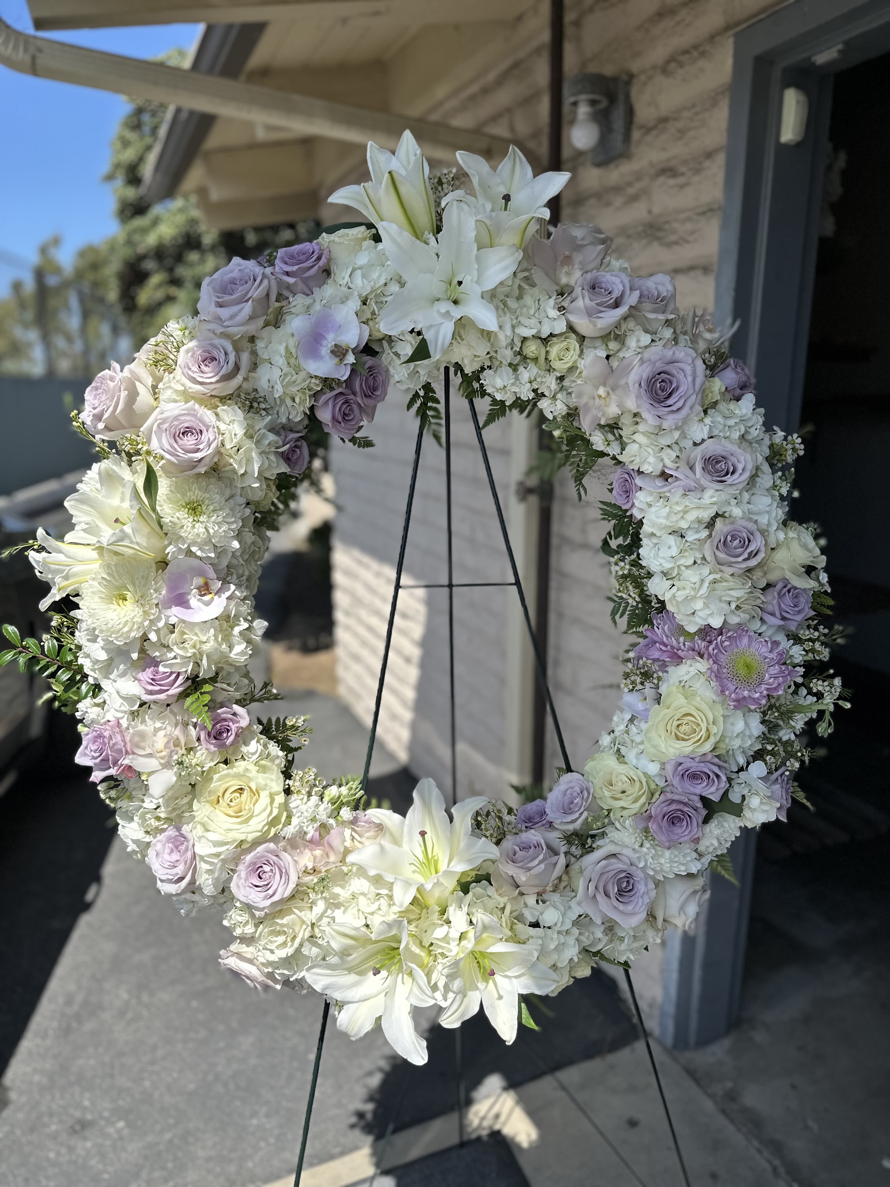 Pacific View Lavender Serenity Wreath - A graceful 30-inch wreath designed in soothing shades of lavender and soft purple. This lush tribute features layers of roses, lisianthus, delphinium, and accents of seasonal blooms, symbolizing eternal love and remembrance. The circular design represents continuity and peace, offering a tender expression of sympathy for services at Pacific View and throughout Orange County.