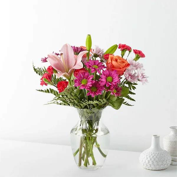 Light of My Life Bouquet - The Light of My Life Bouquet blossoms with brilliant color and a sweet sophistication to create the perfect impression! Pink Lilies make the eyes dance across the unique design of this flower bouquet, surrounded by the blushing colors of orange roses, lavender cushion poms, hot pink carnations, and lush greens. Presented in a clear glass vase, this fresh flower arrangement has been created just for you to help you send your sweetest thank you, happy anniversary, or thinking of you wishes.  Details 19&quot;h x 17&quot;w  Bloom Details Carnation Lily Rose