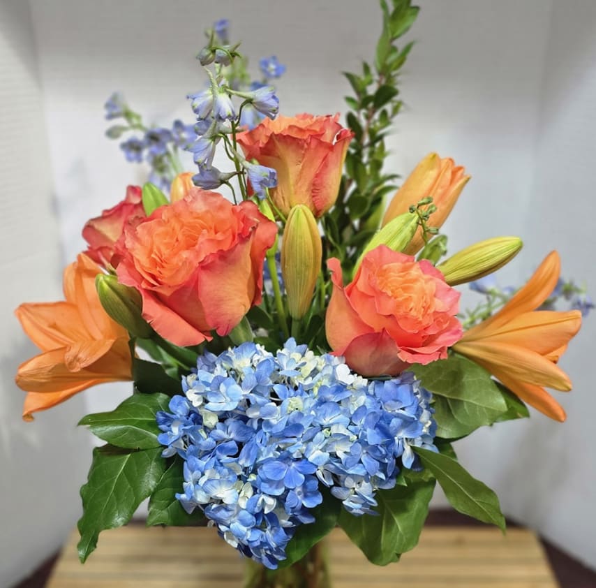 Tropical Twilight - Bring the beauty of a tropical sunset indoors with our Tropical Twilight Bouquet. Featuring striking blue delphinium, bold orange lilies, soft roses, and lush blue hydrangea, this bouquet dazzles with a vibrant mix of colors and textures—perfect for birthdays, celebrations, or brightening any special occasion.  Hand-arranged with care and accented with fresh greenery, each bloom is chosen for its freshness and vibrancy. Delivered with love by Adorkable Flowers and Gifts, the Tropical Twilight Bouquet is a stunning gift that captures attention and inspires joy.  *Some stages of flower life may vary. (Example: Lilies may be more open than imaged.)  Flower shortages and product availability means that some substitutions will apply. Value will always be filled.  This bouquet might include eucalyptus amongst the greenery. It may be toxic to pets including but not limited to Cats and Dogs if digested.