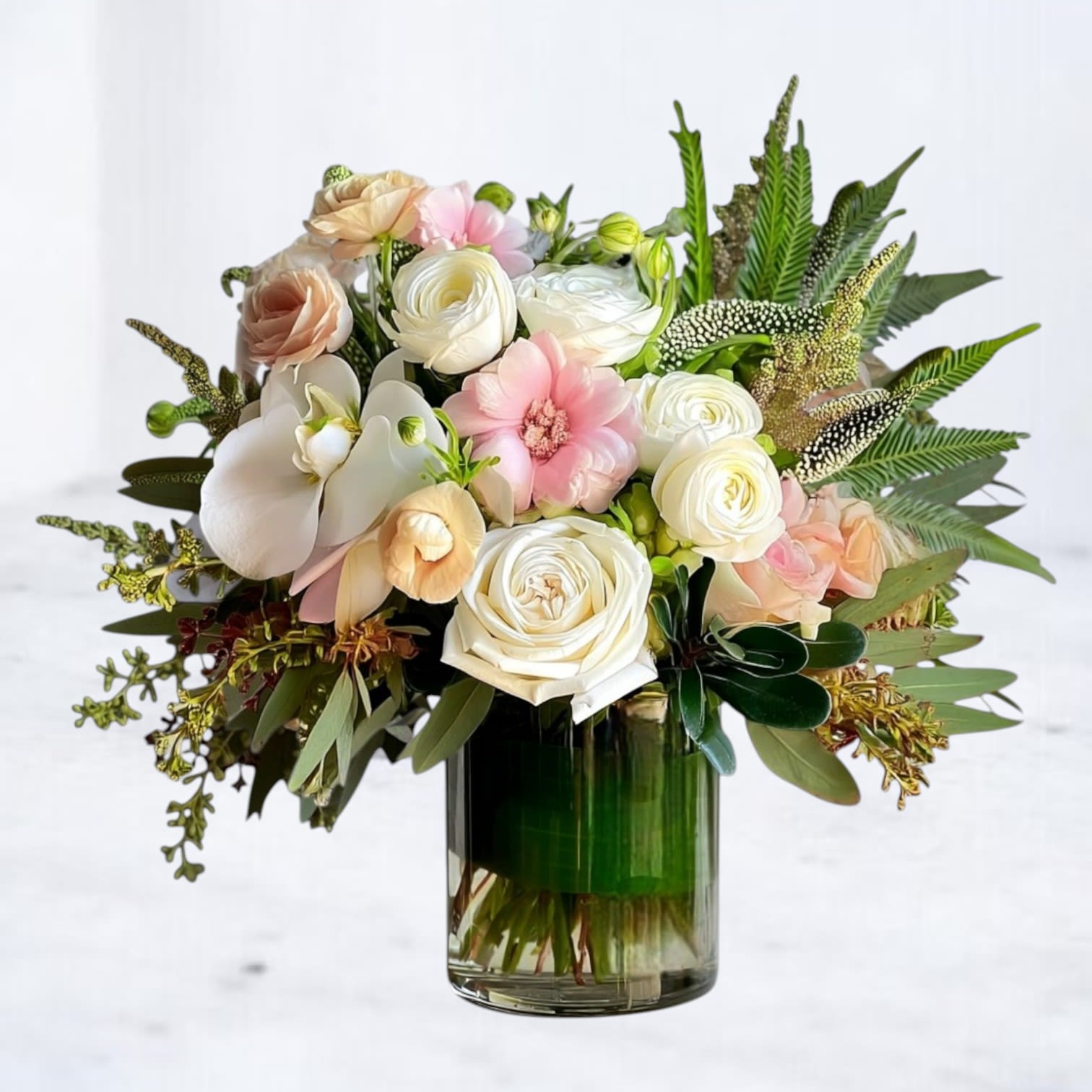Silken Still Silken Still - Understated and serene, Silken Still is a refined floral arrangement that whispers elegance. This peaceful design features creamy white roses, pale blush lisianthus, ranunculus, orchids, and delicate greenery—gracefully arranged in a leaf-wrapped glass vessel. The soft textures and gentle tones create a sense of quiet luxury and effortless calm.