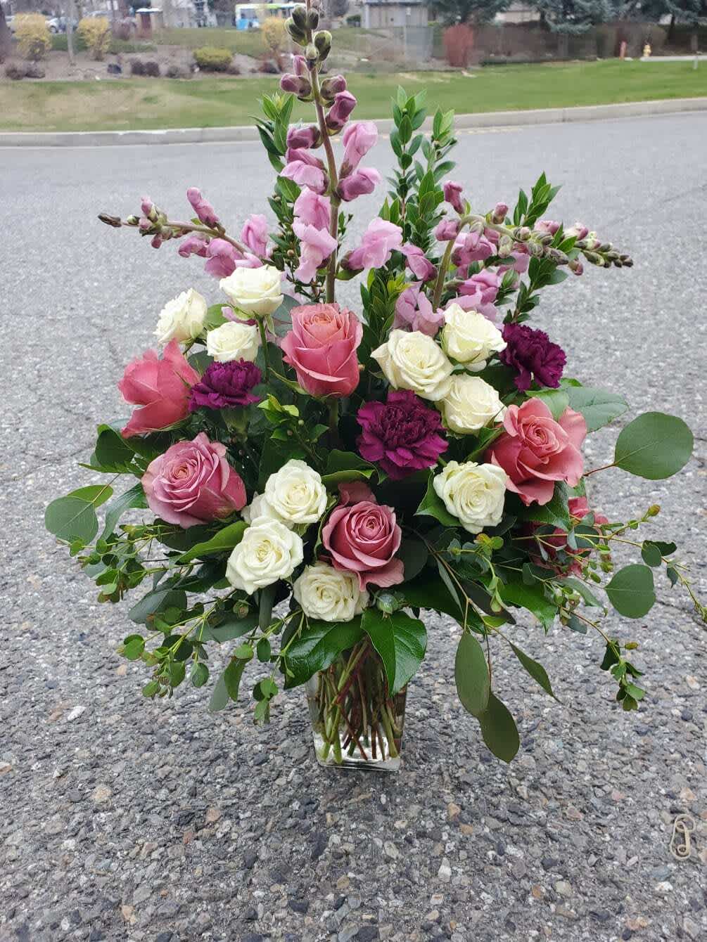 Calista Rose - Bring the charm of the countryside indoors with our Calista Rose Bouquet, featuring serene country blue roses, delicate white spray roses, vibrant fuchsia carnations, elegant snapdragons, and a lush mix of lemon leaf greens and eucalyptus. This delightful combination of colors, textures, and fragrances creates a cheerful and sophisticated bouquet, perfect for birthdays, celebrations, or brightening someone’s day.  Hand-selected for freshness and carefully arranged, each bloom is showcased to highlight its natural beauty. Delivered with care by Adorkable Flowers and Gifts, the Calista Rose Bouquet is a thoughtful gift that radiates joy and elegance.   * Some stages of flower life may vary. (Example: Lilies may be more open than imaged.)  Flower shortages and product availability means that some substitutions will apply. Value will always be filled.  This bouquet might include eucalyptus amongst the greenery. It may be toxic to pets including but not limited to Cats and Dogs if digested.