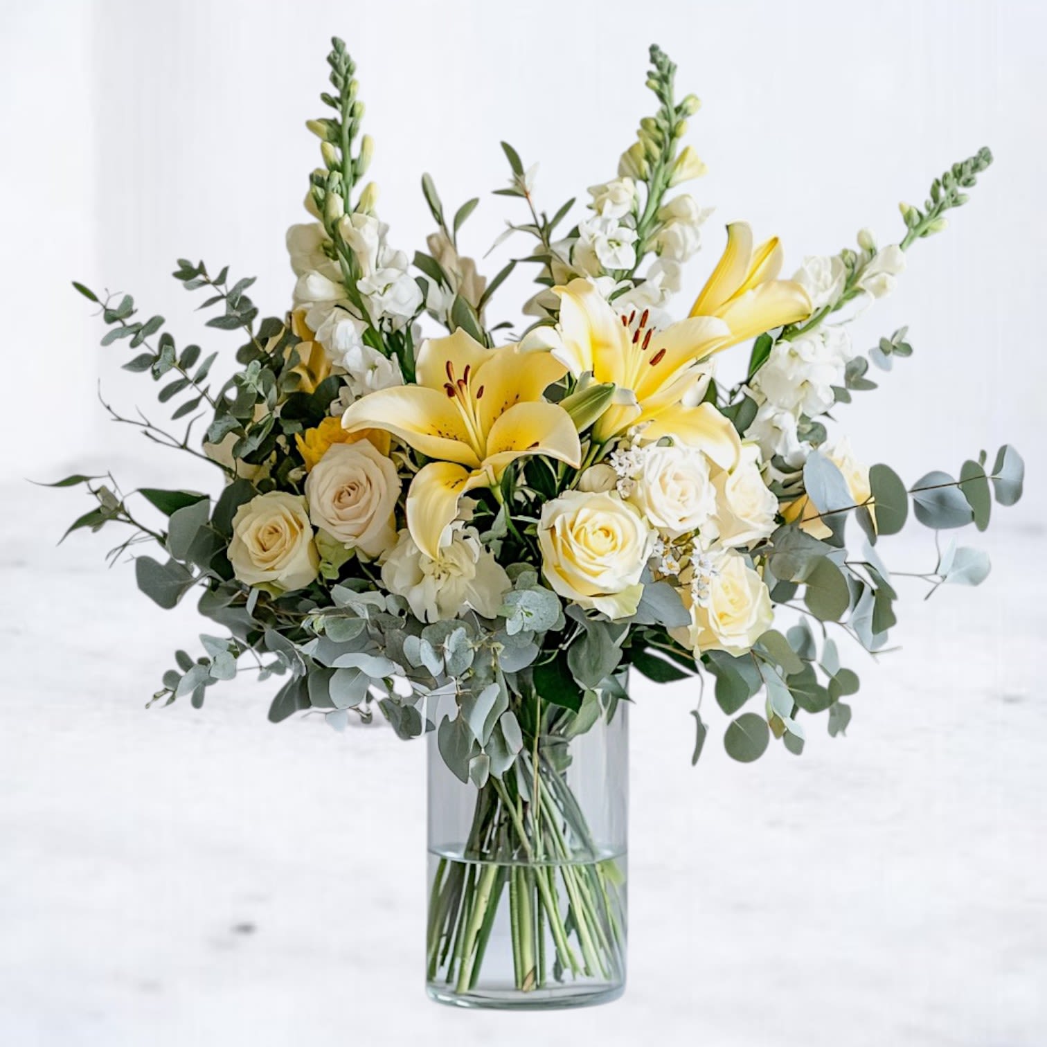 Sunlit Remembrance Sunlit Remembrance - Honor cherished memories with our Sunlit Remembrance sympathy flower arrangement, a graceful blend of fresh yellow lilies, creamy white roses, snapdragons, and lush eucalyptus. Designed to bring warmth and peace, this elegant floral display offers comfort during times of loss, symbolizing hope, remembrance, and everlasting love. Perfect for funeral services, memorials, or as a heartfelt condolence gift, our expertly crafted bouquet is available for same-day sympathy flower delivery across Houston, Magnolia, The Woodlands, Conroe, Cypress, and surrounding areas. Each stem is thoughtfully selected for its beauty and longevity, ensuring a stunning tribute that speaks when words fall short.