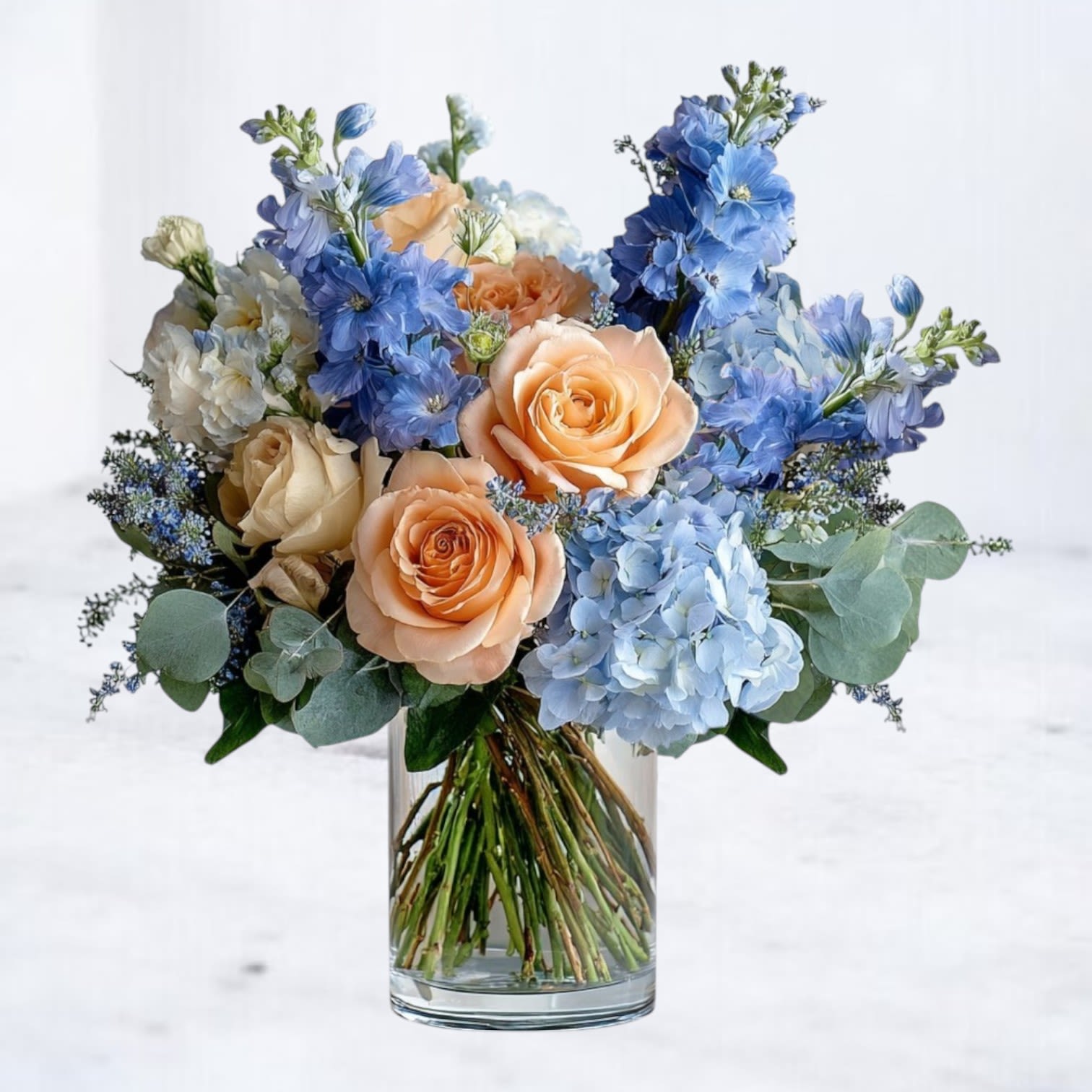 Morning Light Bouquet Morning Light Bouquet - The Morning Light Bouquet captures the serene beauty of a new day with its pastel blend of peach roses, creamy ivory blooms, and soft blue hydrangeas. Accented with delicate white stock and fresh eucalyptus, this arrangement is designed in a clear glass vase for a modern yet timeless look. Perfect for birthdays, anniversaries, welcoming a new baby, or simply brightening someone’s day, this bouquet radiates warmth and joy with every petal. Available for same-day flower delivery in Houston, Magnolia, The Woodlands, Spring, Conroe, and surrounding areas.