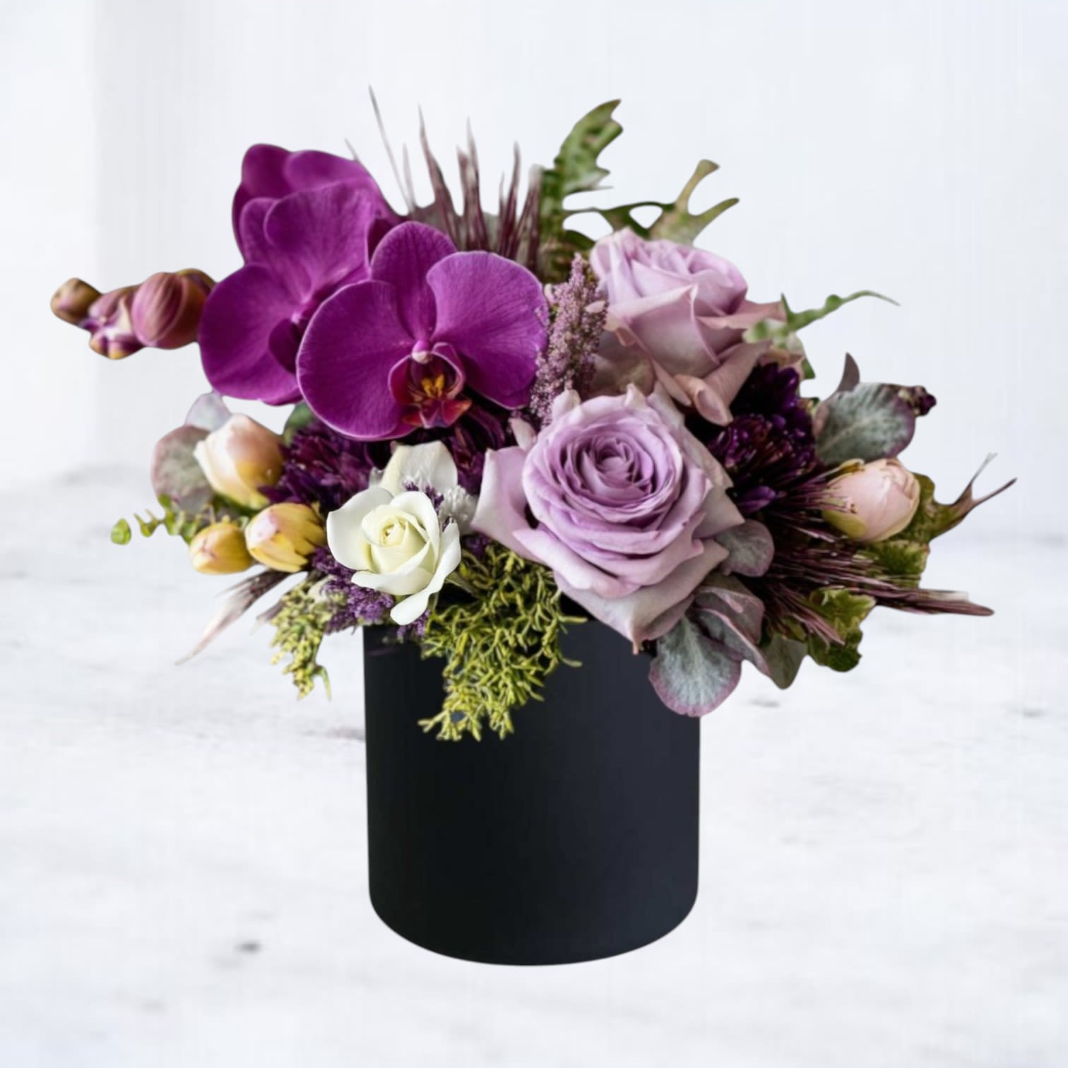 Noir Eclipse Bouquet Noir Eclipse Bouquet - Our Noir Eclipse Bouquet is a bold and captivating floral statement, blending deep plum orchids, lavender roses, and creamy ivory blooms against lush modern greenery. Designed in a sleek matte black vase, this luxury arrangement embodies elegance with a dramatic edge. Perfect for anniversaries, sympathy tributes, or upscale gifting, Noir Eclipse offers a couture-inspired aesthetic that sets it apart. Available for same-day flower delivery in Houston, Magnolia, The Woodlands, and surrounding areas.