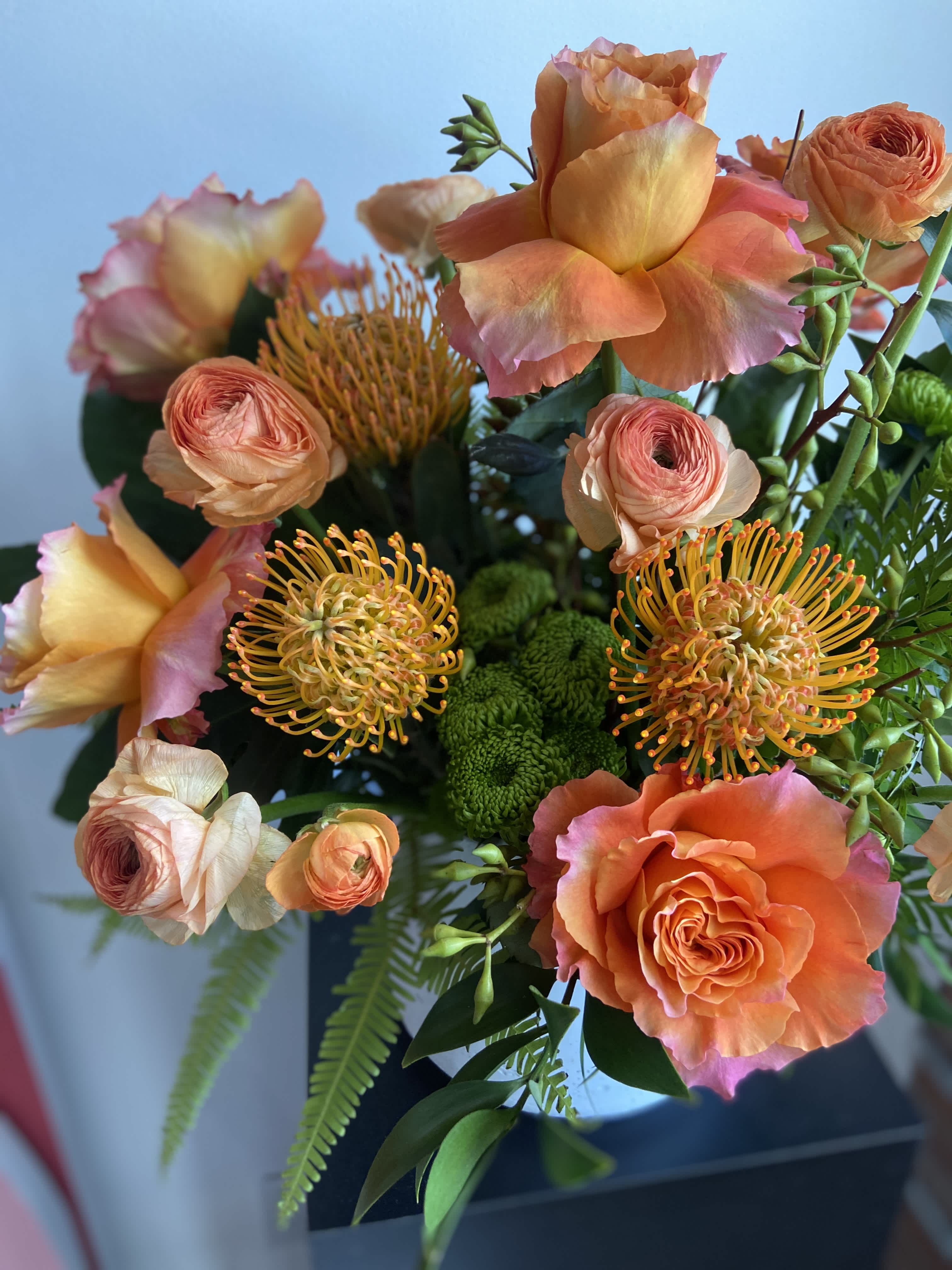 Orange Crush - This statement piece is your perfect dose of Vitamin C! Bursting with Ruffled Free Spirit Roses, Protea, Ranunculus, and Ferns. A guaranteed crush!