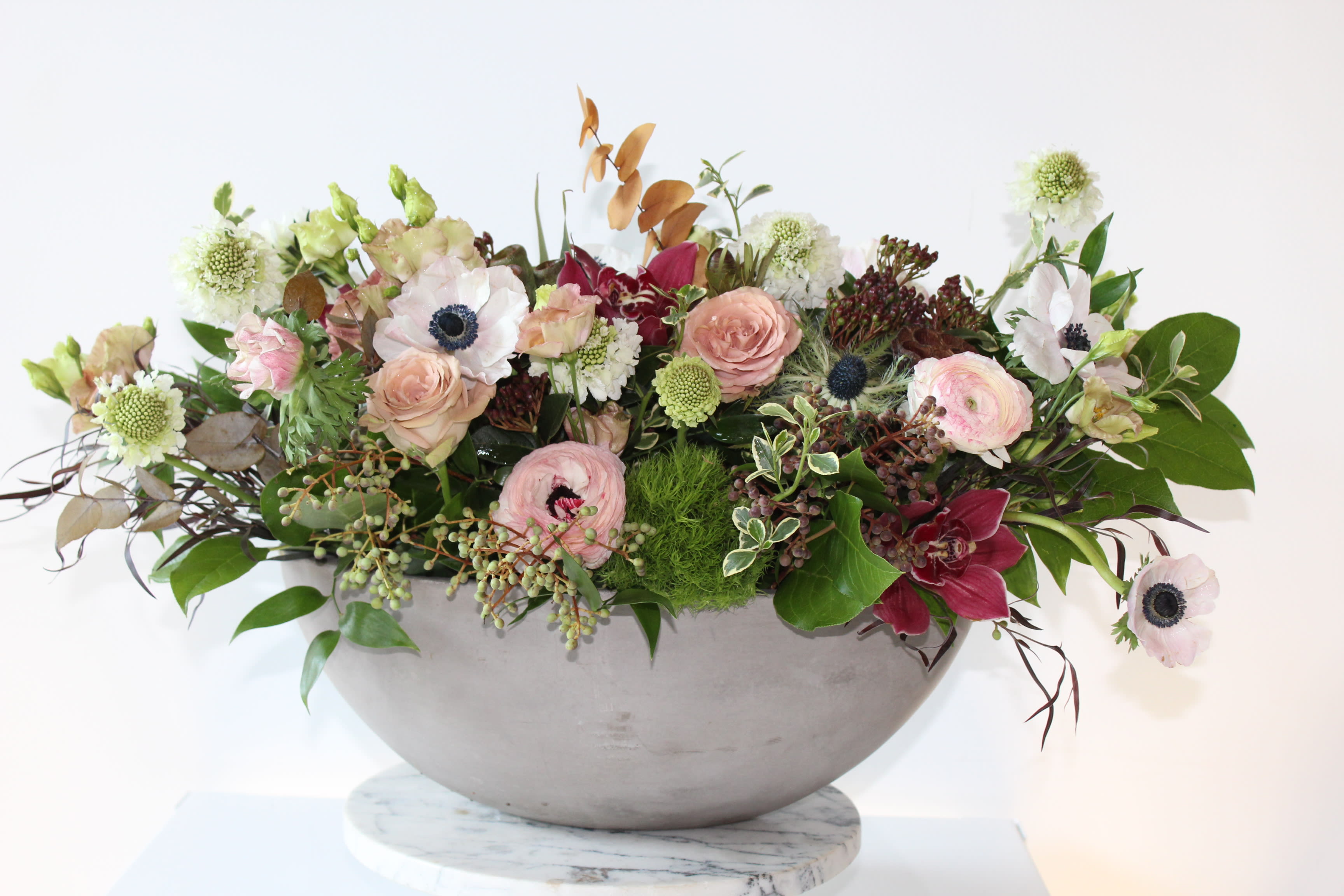 The Carruth The Carruth - For the Modern Home. This sleek and sophisticated centerpiece is bursting with luxe blooms, Including: Cappuccino Roses, Anemones, and Italian Ranunculus. Perfect size for any dining table or kitchen island.