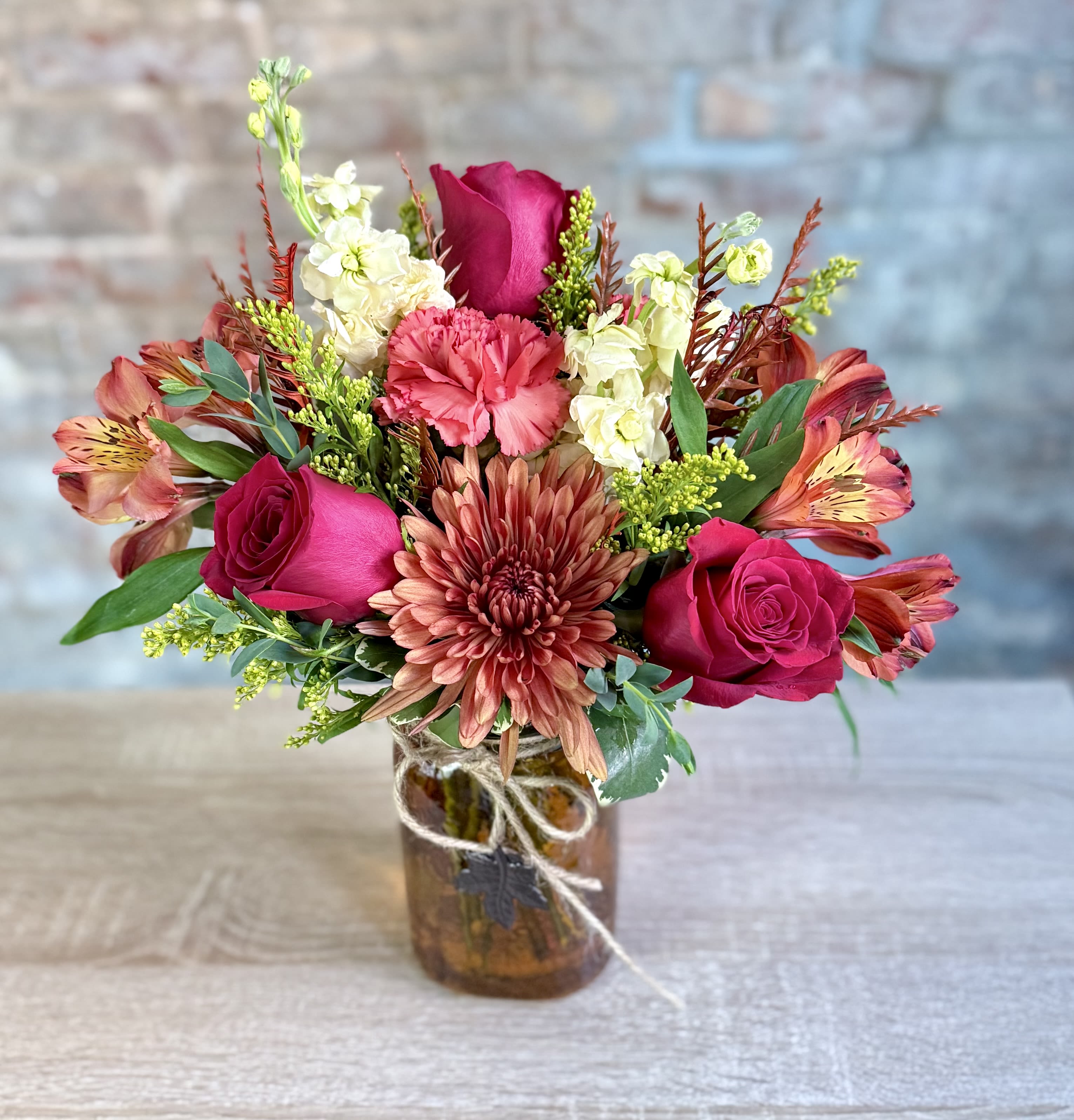 Autumn Leaves Autumn Leaves - A cute colored glass jar with a metal leaf hanging in the front. Filled with fall colored blooms, cremon, alstroemeria, red roses, cream stock and grevellia make up this pretty fall arrangement.