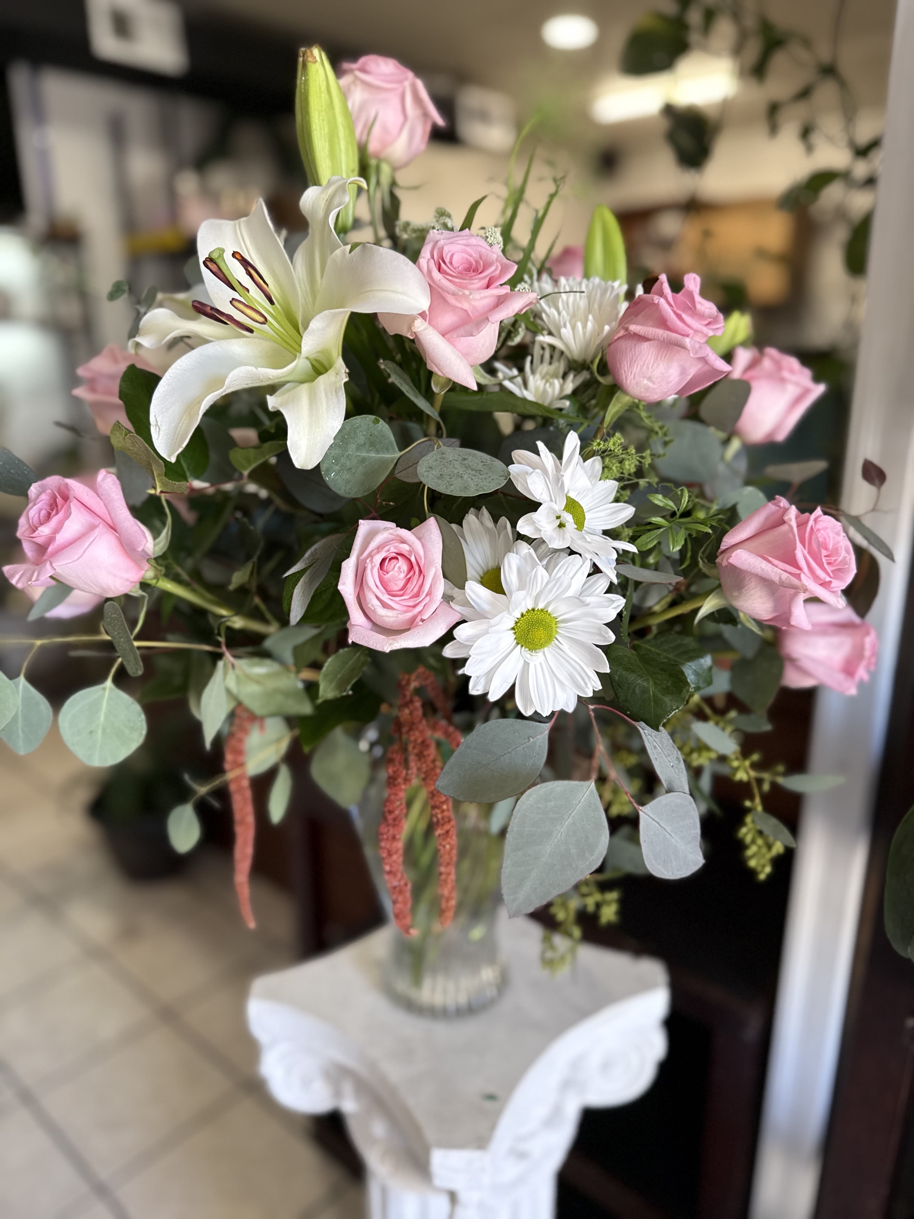 Blushing Elegance Bouquet Blushing Elegance Bouquet - Capture a moment of pure grace with our Blushing Elegance Bouquet. This exquisite arrangement is a symphony of soft color and classic beauty, designed to convey warmth and affection. Inside, you'll find velvety pink roses, the timeless symbol of romance and appreciation, harmoniously blended with fragrant, star-shaped white lilies that add a touch of sophistication. Cheerful white daisies are sprinkled throughout, lending a light and airy feel, while the gentle, aromatic leaves of silver dollar eucalyptus provide a modern, textural backdrop. Presented in a simple yet elegant clear glass vase, this bouquet is perfect for anniversaries, birthdays, thank-you gestures, or any occasion that calls for a truly special and heartfelt gift.