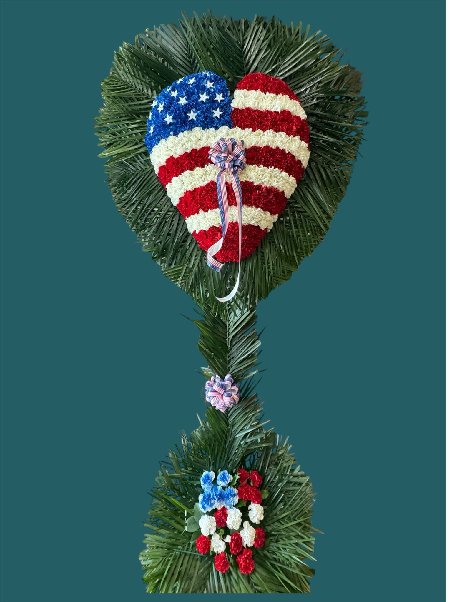 Patriotic Carnation Heart  - A patriotic floral arrangements with red, white and blue blooms over palm leaves.