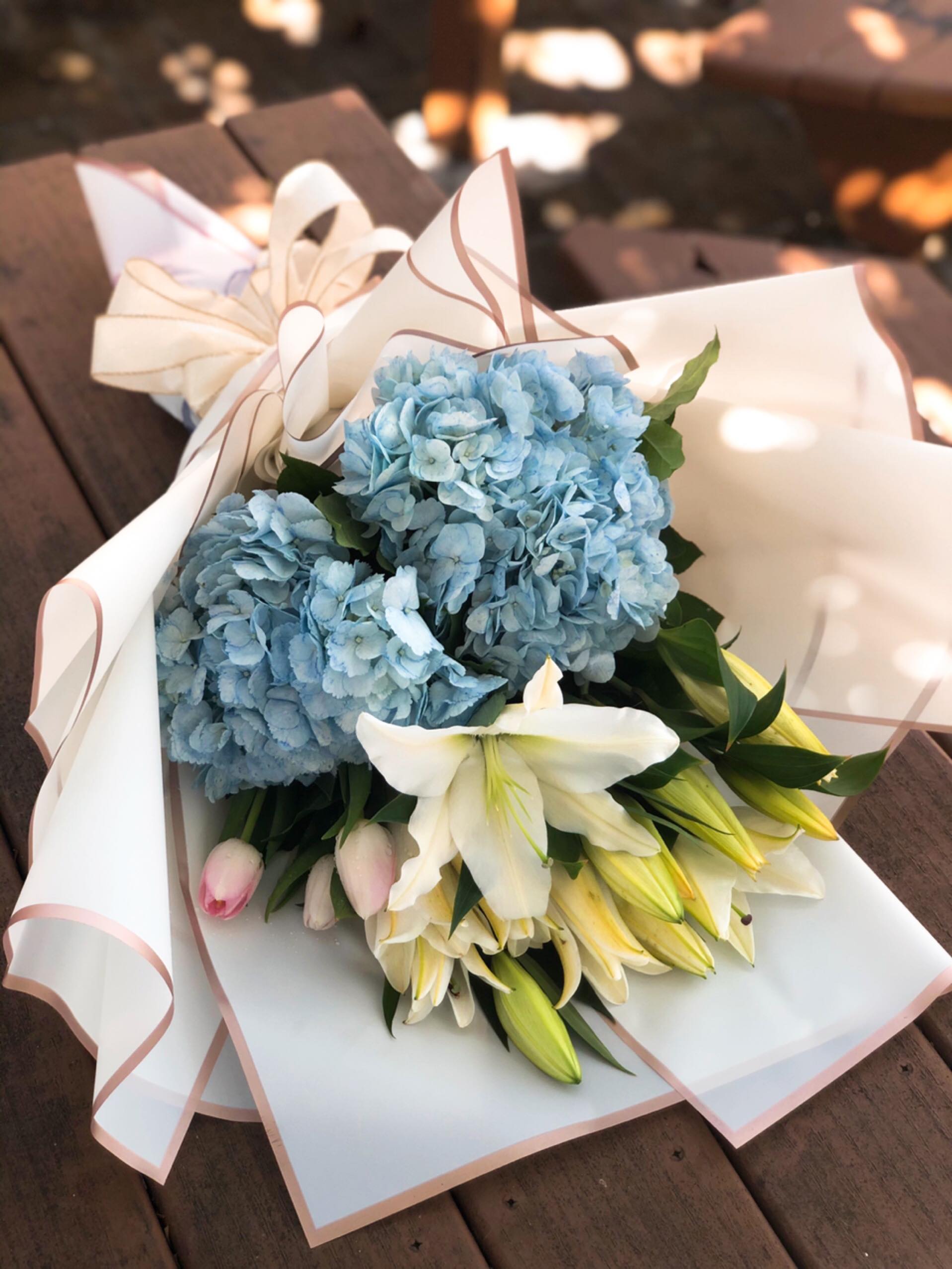 Hydrangeas w/ Lilies and Tulips Wrap Hydrangeas w/ Lilies and Tulips Wrap - - 2 Blue Hydrangeas - 4 Stems White Lilies - 3 Stem pink tulip - Greenery - Papers And Bow