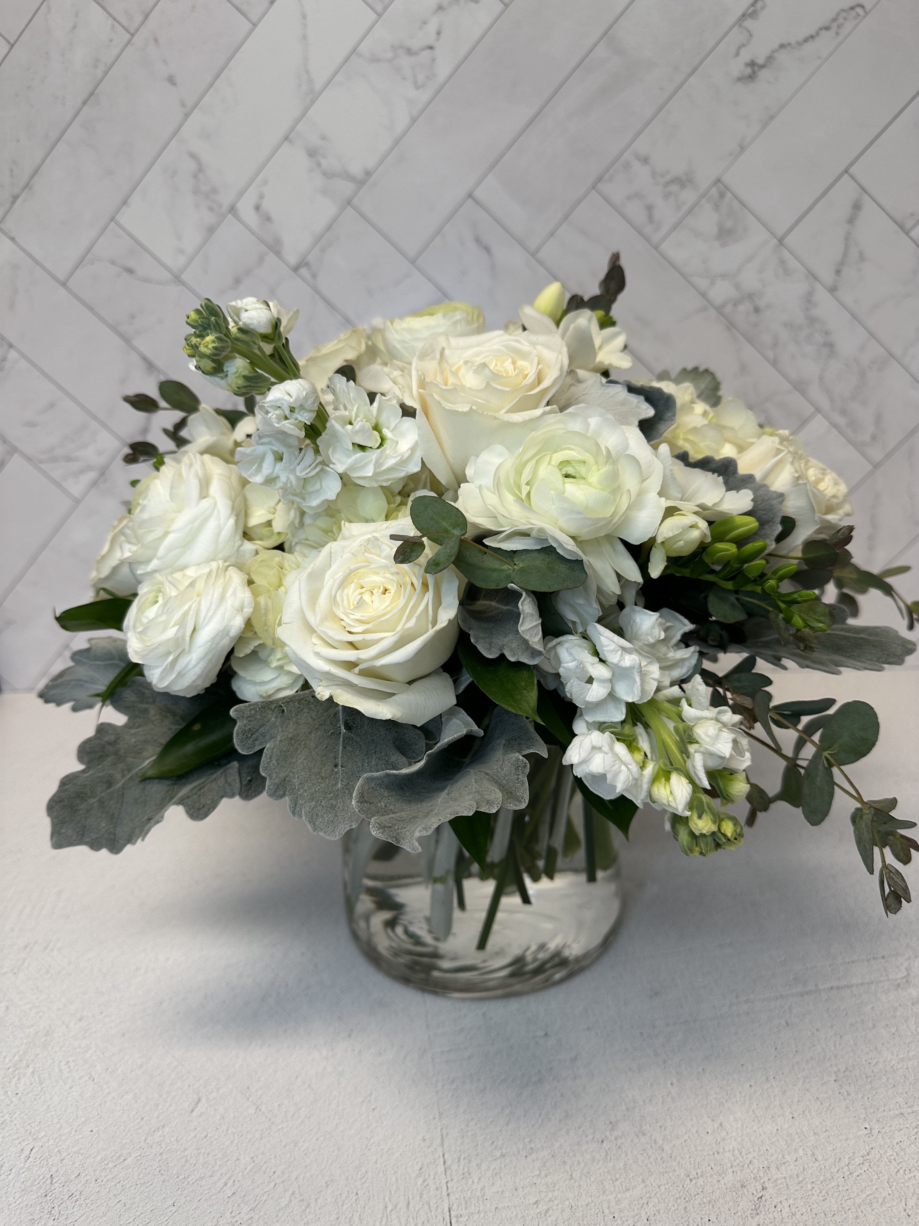 White Sensation - White Sensation- a timeless arrangement in a clear vase (available in 5,6, or 8 diameter). Featuring white hydrangeas, roses, ranunculus, freesia, and stock accented with elegant greenery. A perfect choice for any occasion.
