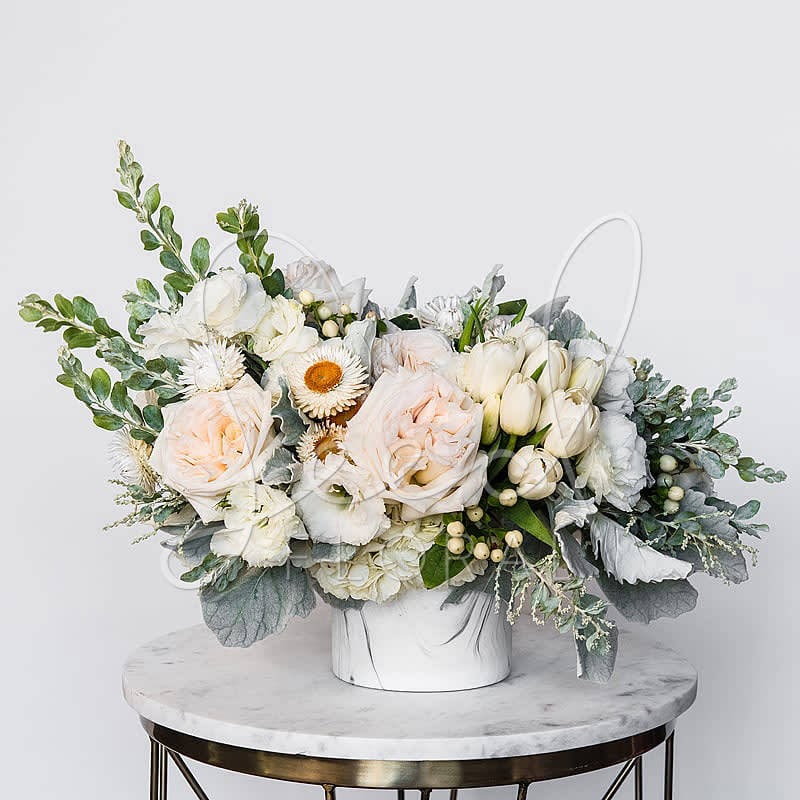White O'Hara - Elevate any space with the timeless elegance of the White O’Hara, a premium floral arrangement featuring the coveted White O’Hara garden rose—known for its large, ruffled petals and soft blush center. This sophisticated design blends fresh white tulips, lisianthus, hydrangeas, strawflowers, and seasonal greenery like eucalyptus and dusty miller, all thoughtfully arranged in a chic marble ceramic vase.  Perfect for weddings, anniversaries, sympathy gifts, luxury home décor, or modern event centerpieces, the White O’Hara arrangement brings softness, texture, and a refined aesthetic to any setting.