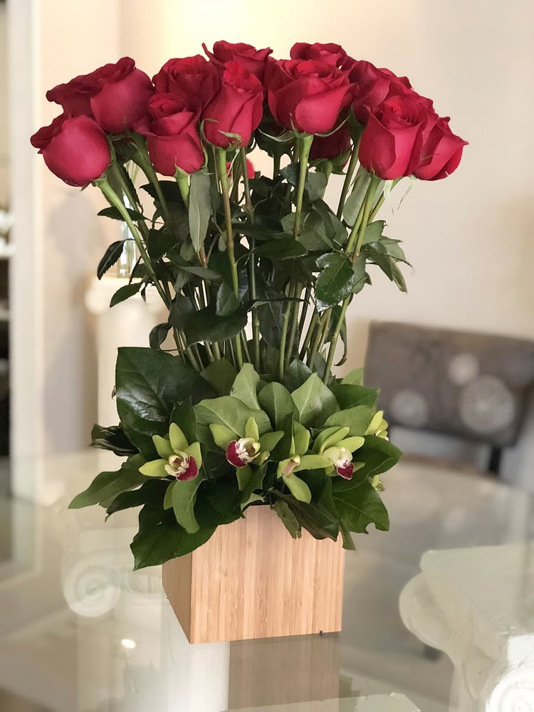 China Basin Romantic Reds - A unique presentation of 24 long-stemmed, ruby-red Roses, in a beautiful base of apple-green Orchid blossoms and leafy greens in a cubical bamboo box.