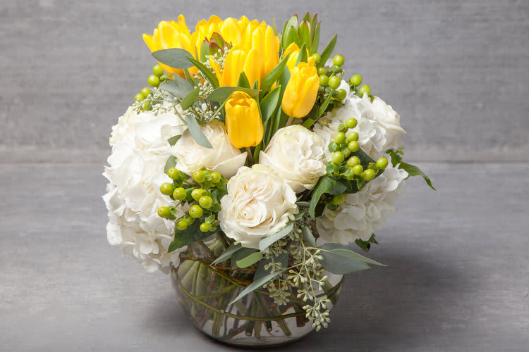 South Beach Spring - A fresh and happy arrangement of golden yellow tulips, linen white blossoms and spring greens produces big smiles.  