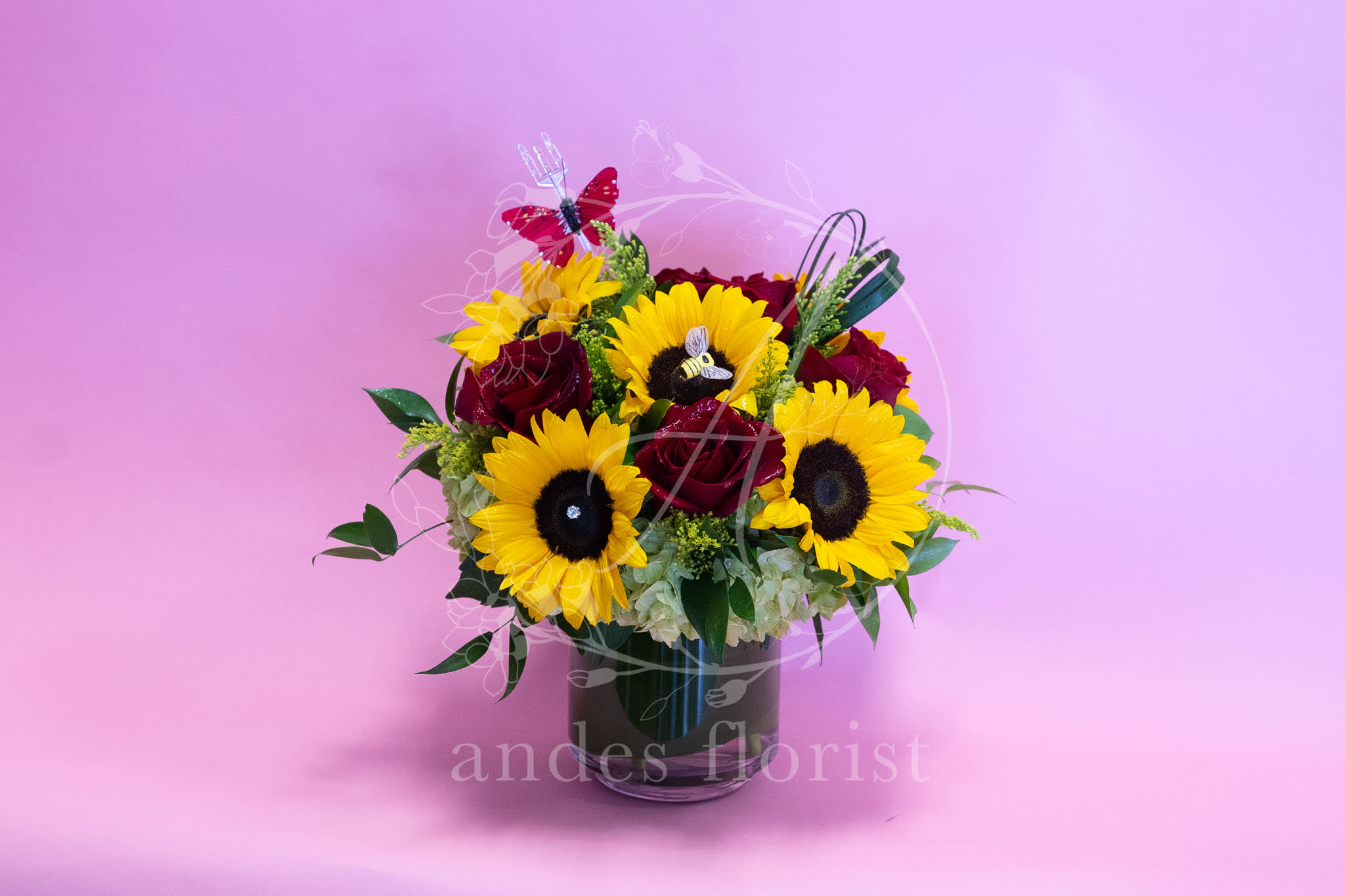Sunflower Lovers Sunflower Lovers - Roses are beautiful but pair them up with sunflowers and you get a bright ray of fun love and sunshine. We're getting cheesy over here, but really, we love combining roses with sunflowers! In a ti-leaf lined vase with a little bee accent hidden in one of the sunflower blooms, this design is full of surprises!