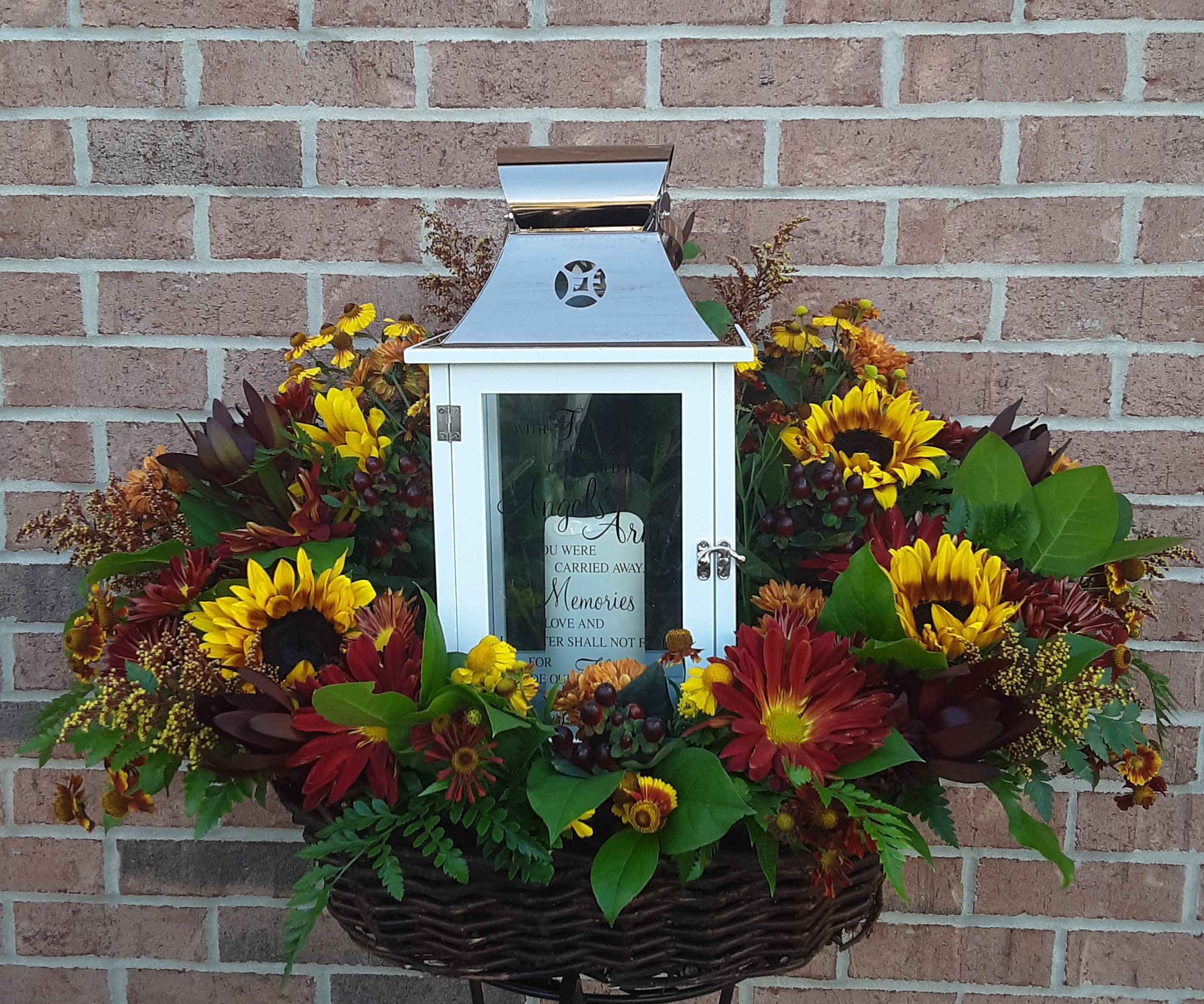 Grande Lantern Arrangement Grande Lantern Arrangement - Any of our largest and most exquisite "Grande" Lanterns will be nestled in an beautiful arrangement of Designer selected seasonal blooms to create an incredible large statement of sympathy. Color selection and bloom choice are at the discretion of the Designer and based on seasonality and availability. Lantern available is "GONE YET NOT FORGOTTEN GRANDE LANTERN and contains a flameless LED candle and is made from quality wood and a stainless steel copper finish top.  It is equipped with a built-in automatic timer and 3 AAA batteries.