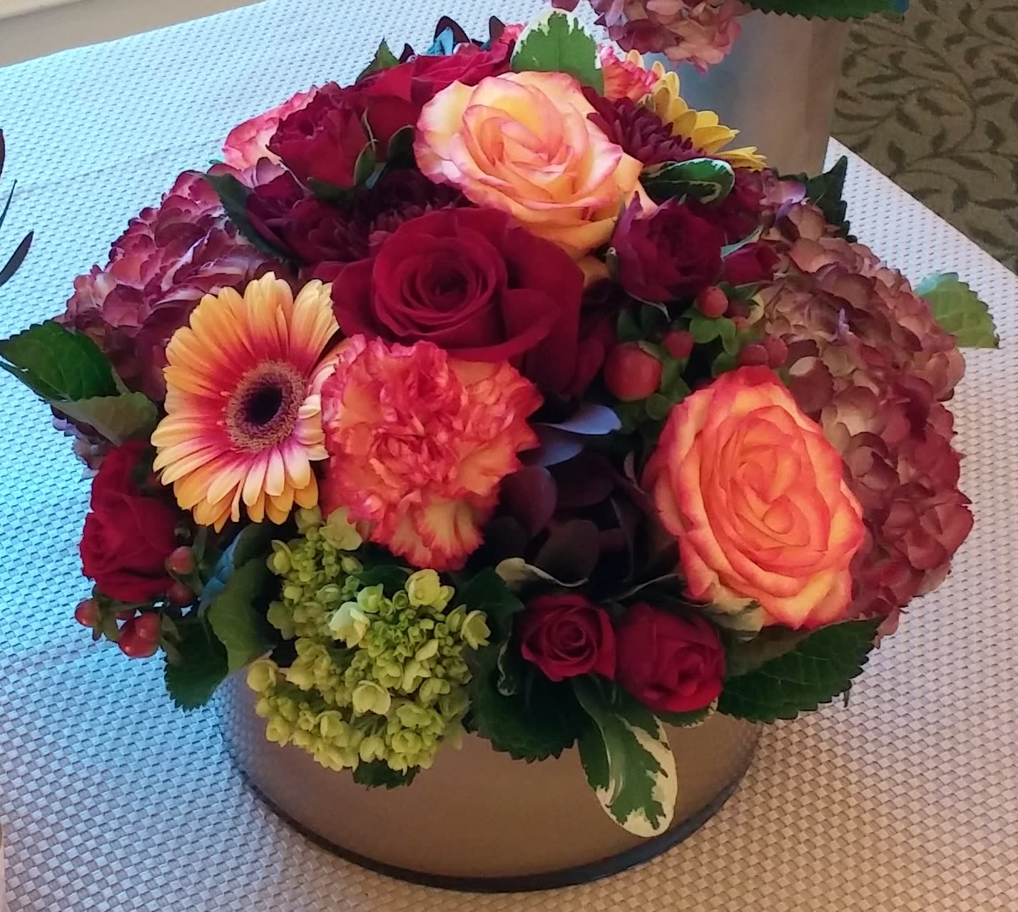 Gather 'Round Centerpiece Gather 'Round Centerpiece - This exquisite centerpiece is styled artistically in a ROUND CONTAINER which is chosen by the designer (Gold container pictured not available at this time). Designer will utilize a collection of beautiful fall colored blooms to craft a lovely lush display of color and seasonality for the Thanksgiving table.