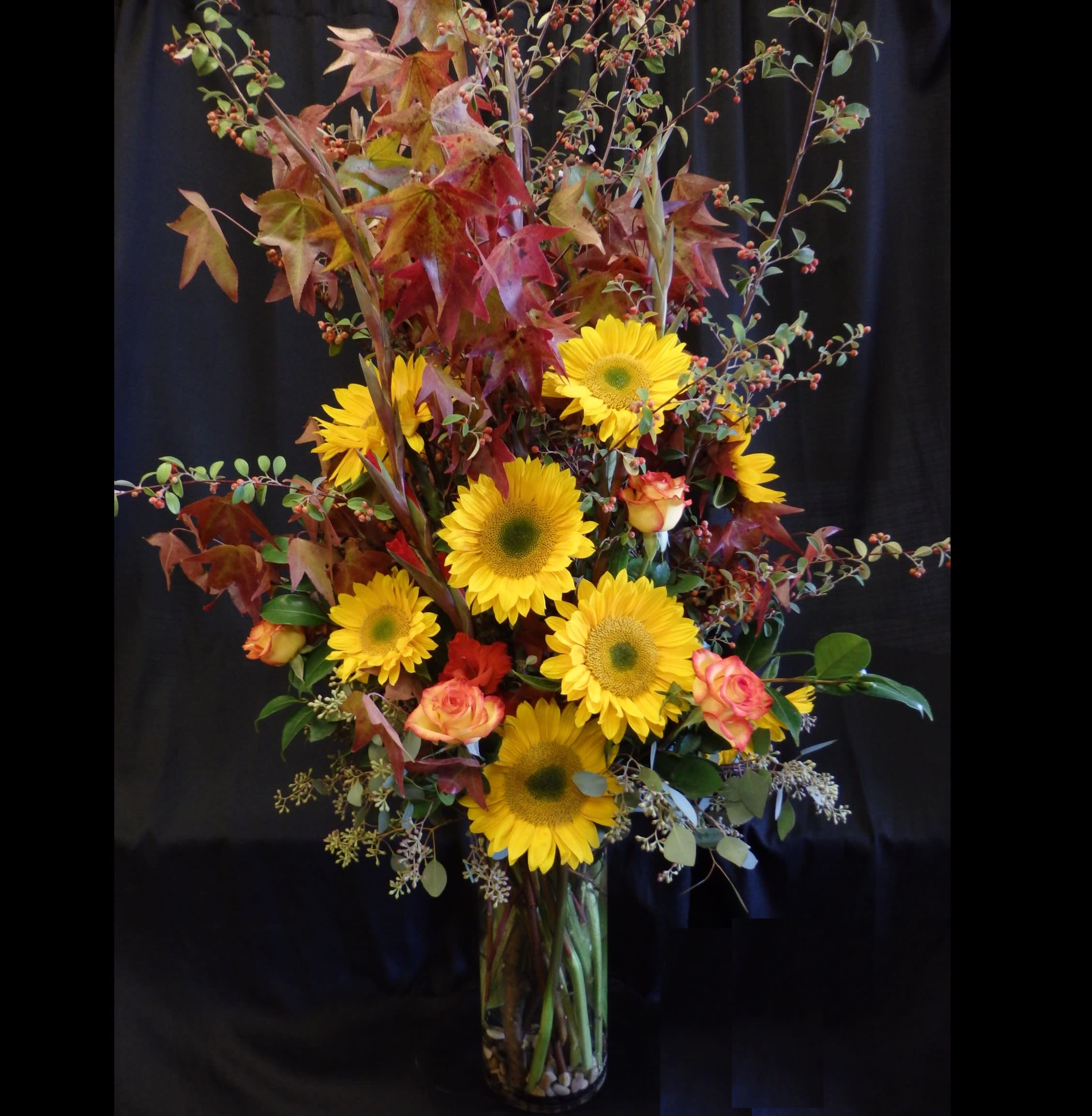 Harvest Garden - &quot;Harvest Garden&quot; is a grand seasonal display featuring golden sunflowers, gladiolas, autumn leaves, and vibrant roses arranged in a tall cylinder glass vase. Bursting with rich fall colors and textures, this striking design brings the beauty of the harvest season to celebrations in Danville, CA.