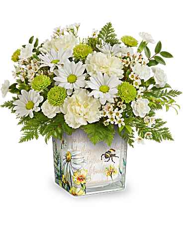 Teleflora's Bee Sweet Bouquet - Celebrate them with this captivating white, light yellow, and green bouquet, elegantly presented in a keepsake glass cube decorated with a charming buzzing bee design. This arrangement features light yellow carnations, white miniature carnations, green button spray chrysanthemums, white daisy spray chrysanthemums, and white waxflower, beautifully complemented by huckleberry and leatherleaf fern. This bouquet is presented in the Floral Buzz cube, a perfect unique piece!