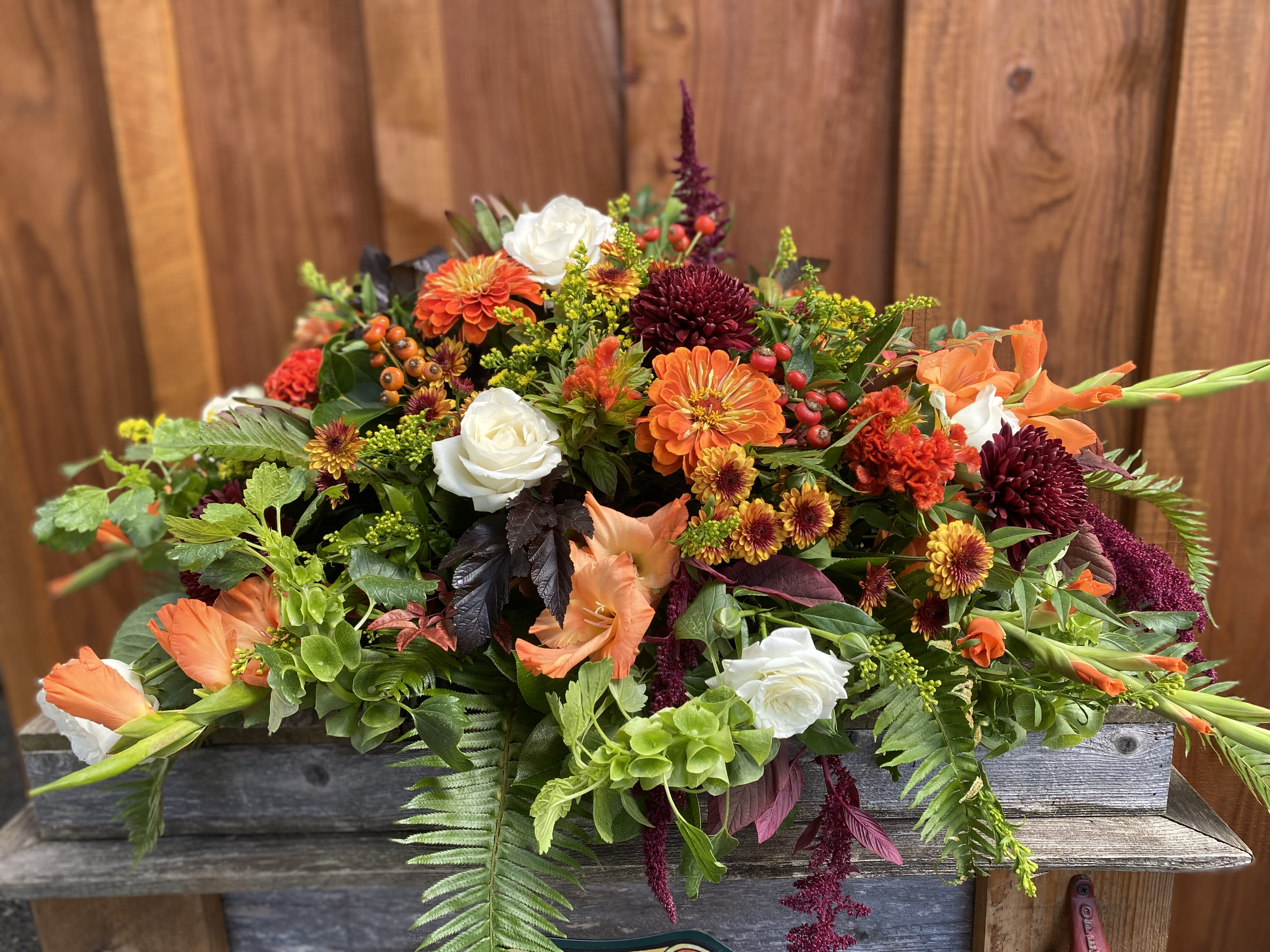 Fall Casket Spray Fall Casket Spray - A perfect way to honor you loved one with an array of the most beautiful colored season of flowers. Roses, mums, snap dragons, amaranthus, bells of ireland and lush native greens make up this beautiful garden.