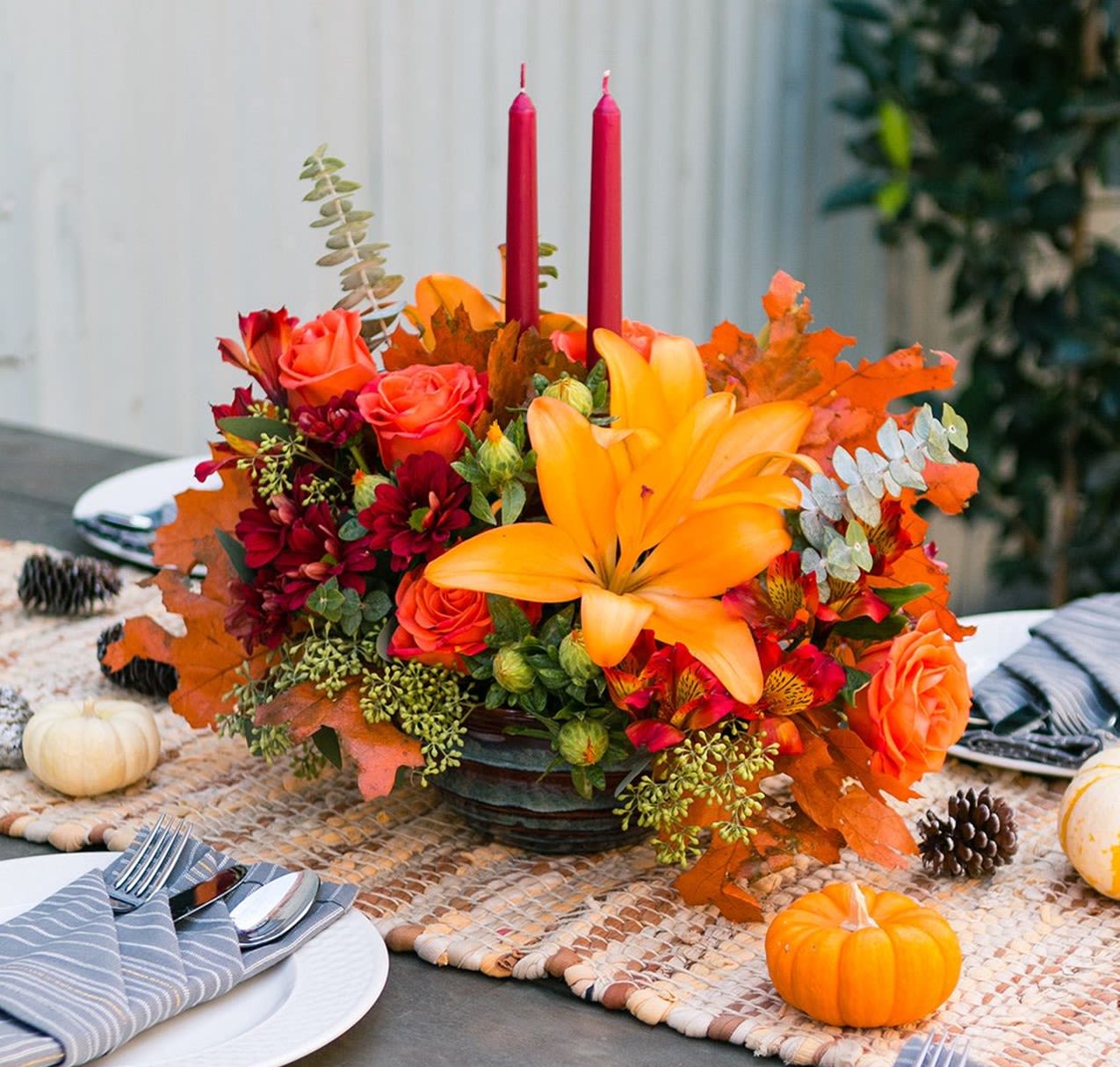 Thanksgiving Traditions - This elegant collection of fall blooms makes the perfect centerpiece for your Thanksgiving get together.  Our professional florists handcraft this arrangement using orange roses, red alstromeria, mini carnations, seeded eucalyptus, baby eucalyptus, red daisies, orange leaves all encompassing elegant  10&quot; red candles.