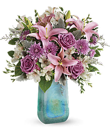 Art Glass Treasure Bouquet - The art of affection! Take her breath away with this beautiful bouquet of lush lavender roses and pink lilies, carefully arranged in a high-fashion, hand-blown art glass vase with swirling iridescent finish. This bouquet features lavender roses, pink asiatic lilies, light pink alstroemeria, lavender cushion spray chrysanthemums, lavender limonium, dusty miller, parvifolia eucalyptus, and lemon leaf.