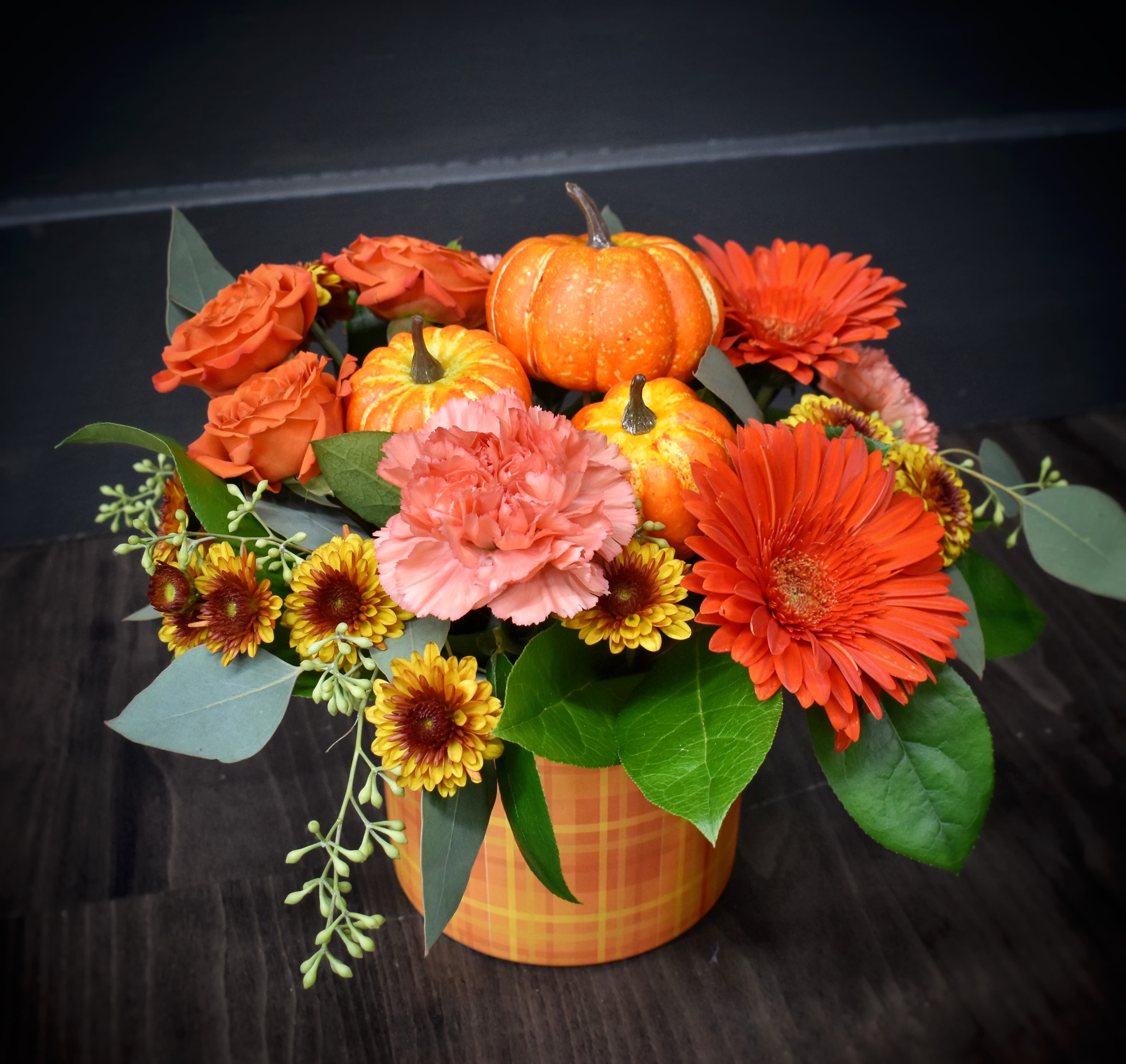 Pumpkin Plaid - A warm gathering of gerbera daisies, mums, spray roses, carnations and a pile of mini silk pumpkins in an orange plaid container. Your own little pumpkin patch!