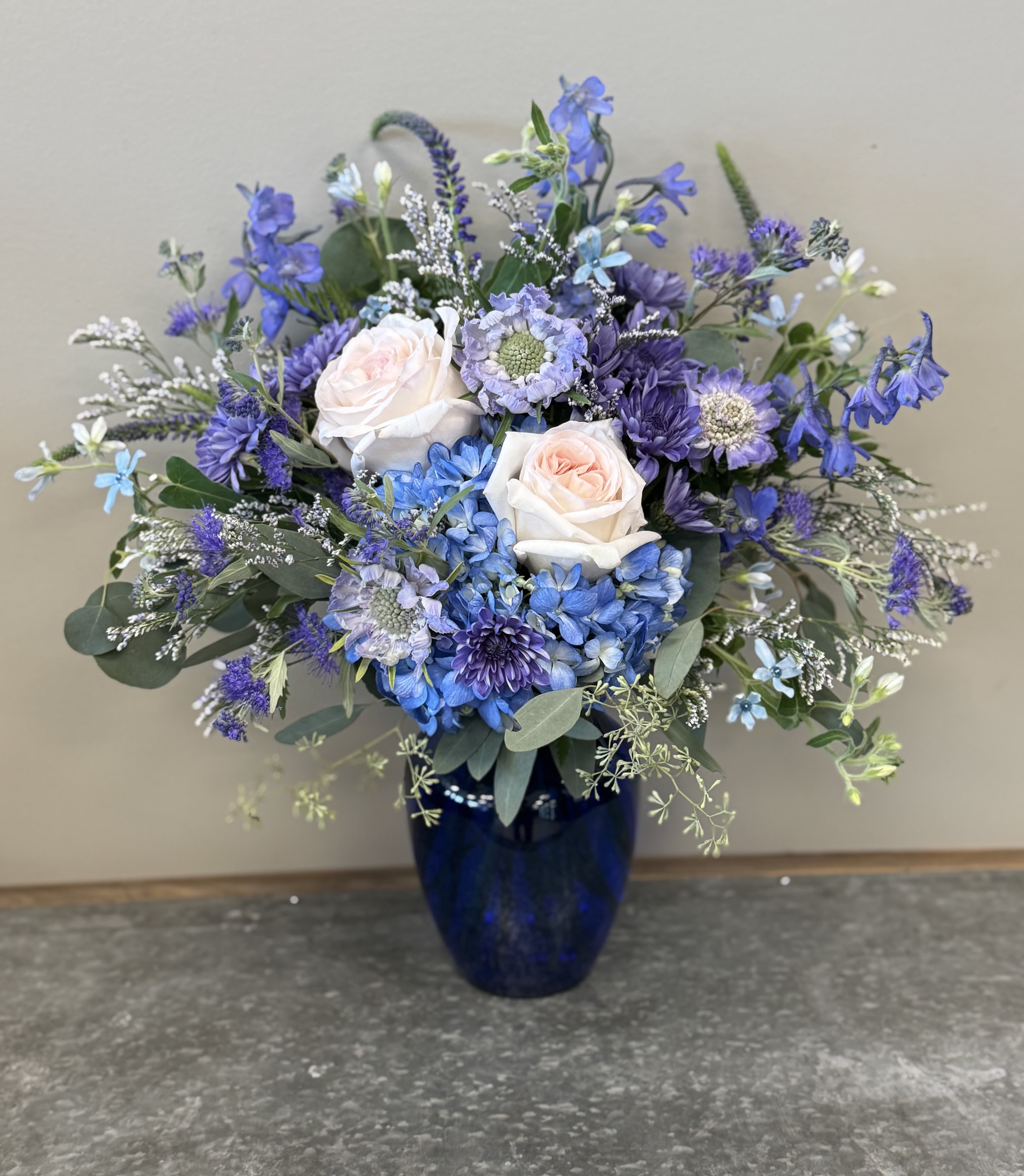 September Sapphire Bouquet - Birthstone Collection What better way to celebrate your loved one's birthday than with our September Sapphire Bouquet! Hand-designed with a stunning gathering of dark and pale blue blooms, soft blushes, silvery eucalyptus greenery, it’s a thoughtful sentiment filled with the noble and wisdom characteristics of a sapphire stone.  ATTENTION! If you are ordering this arrangement on a different month other than what it's respected month is, there will be substitutions for certain flowers depending on seasonal availability. We will stay within the same color scheme and design style!  PLEASE NOTE: Florist reserves the right to make modifications to the design based on seasonality and accessibility of blooms and vases. Any modifications made will honor the palette, intent, and feeling of the pictured design. Contact floral designer directly with any specifications or concerns. 