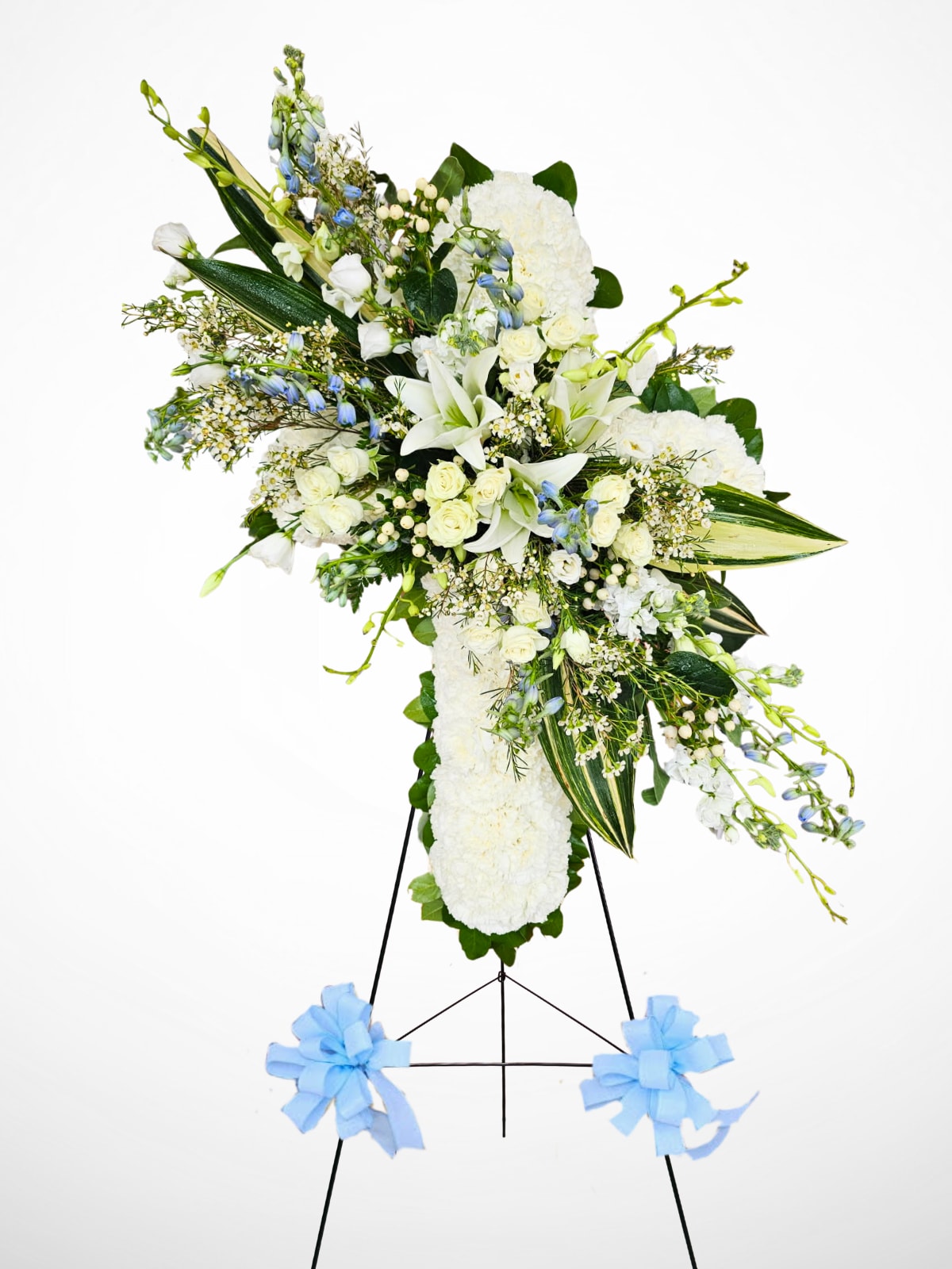 Heavenly Peace Spray - This elegant standing spray is a beautiful tribute of peace and comfort. Designed with white lilies, , berries, roses, stock, wax, orchids, lisianthus, carnations, and delicate blue delphinium, it offers a serene expression of sympathy. Arranged on a standing easel and finished with soft blue bows, this piece conveys heartfelt condolences while honoring the memory of a loved one with grace and dignity.