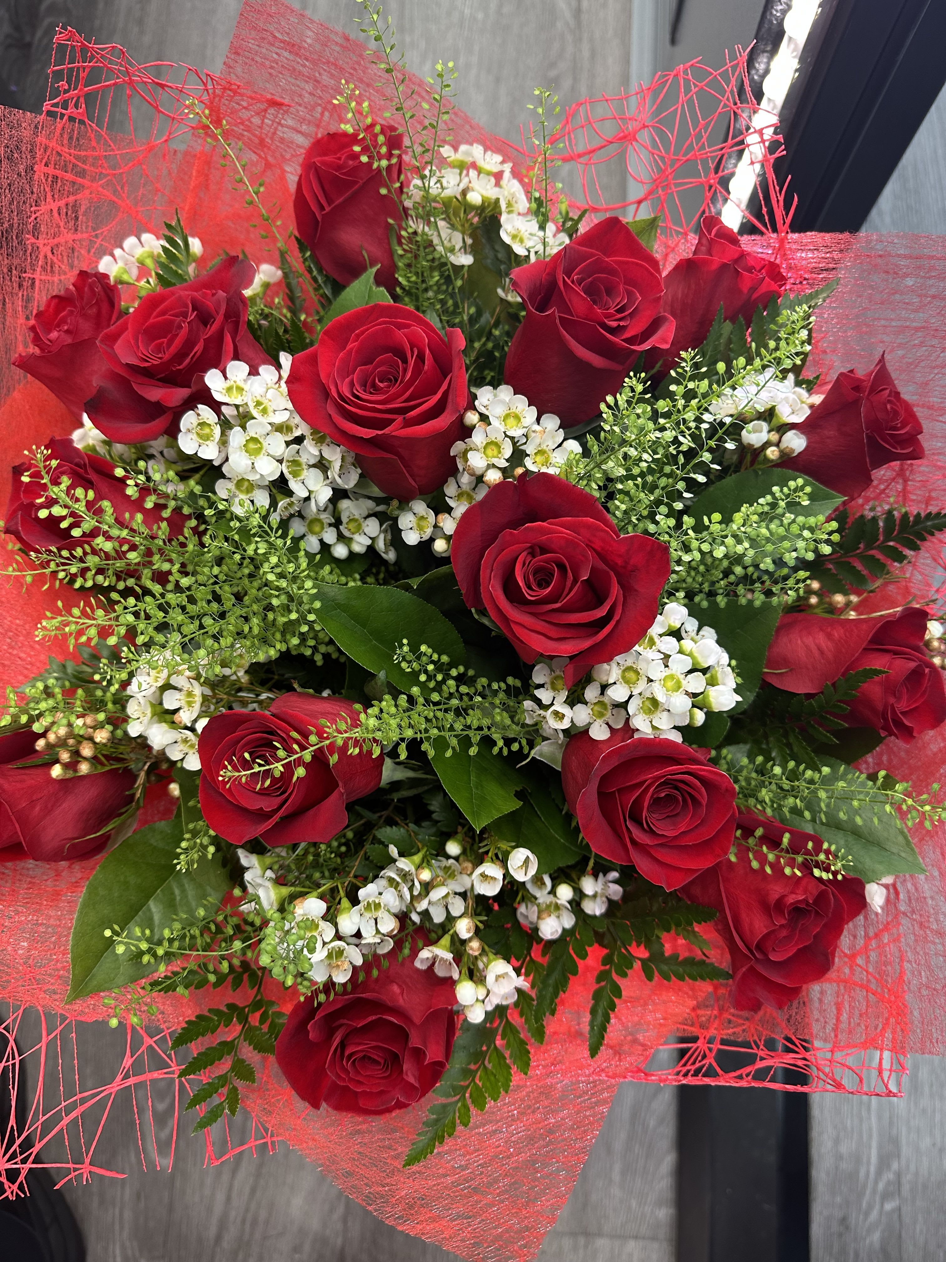 Red Sensation  - A stunning hand-wrapped bouquet featuring vibrant red roses, delicate white wax flowers, and a lush mix of greenery, elegantly wrapped in rich red paper.