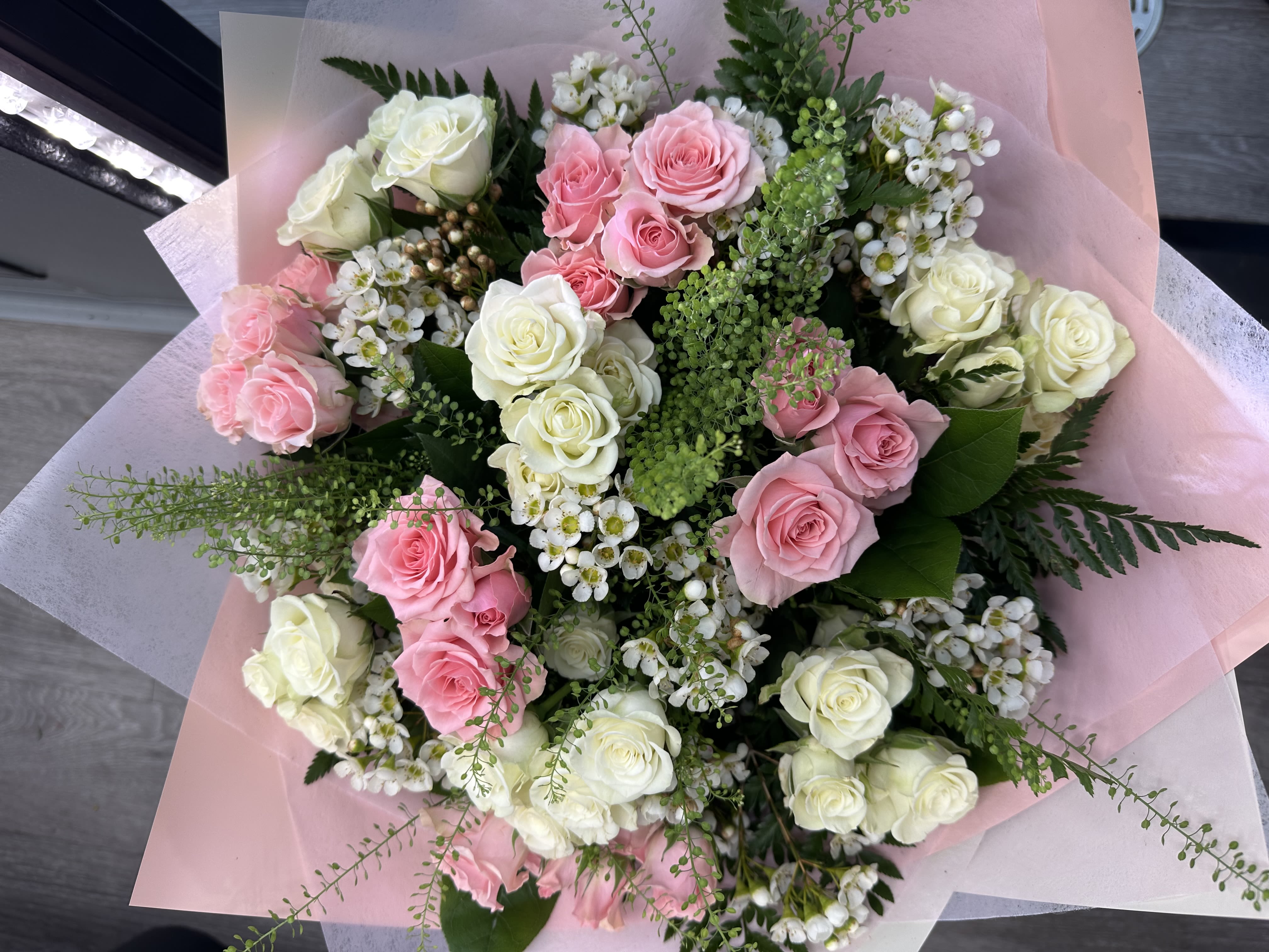 Sweet Elegance - A delicate hand-wrapped bouquet of baby pink and white spray roses, accented with wax flowers and fresh greenery for a soft, romantic look.