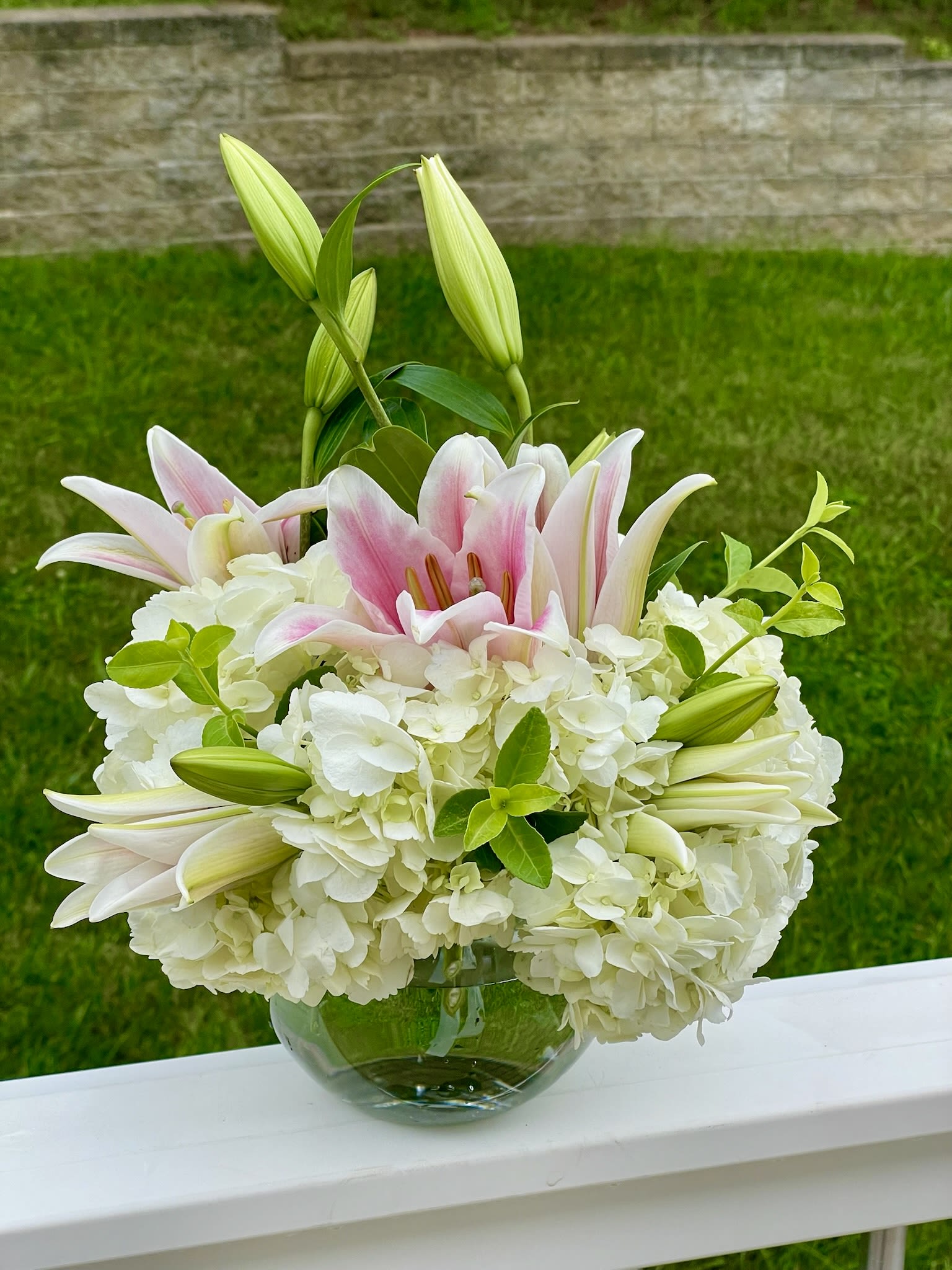 Peaceful Comfort - In moments of sorrow, express your deepest condolences and offer a gesture of peaceful comfort with our &quot;Peaceful Comfort&quot; arrangement. This serene bouquet is thoughtfully designed with elegant white hydrangeas, creating a cloud-like base of gentle support, and accented with graceful pink-and-white stargazer lilies, symbolizing purity, hope, and the beautiful memory of a loved one. Fresh green foliage adds a touch of natural solace.  Measuring approximately 10 inches high and 12 inches wide, this arrangement provides a significant and comforting presence without being overwhelming, making it suitable for a funeral service, a memorial, or as a heartfelt delivery to a grieving family's home.  The delicate beauty and tranquil colors of this arrangement serve as a tender tribute, offering solace and expressing your sincere sympathy.  We understand the importance of timely delivery during these sensitive times and are here to assist you with local delivery services.