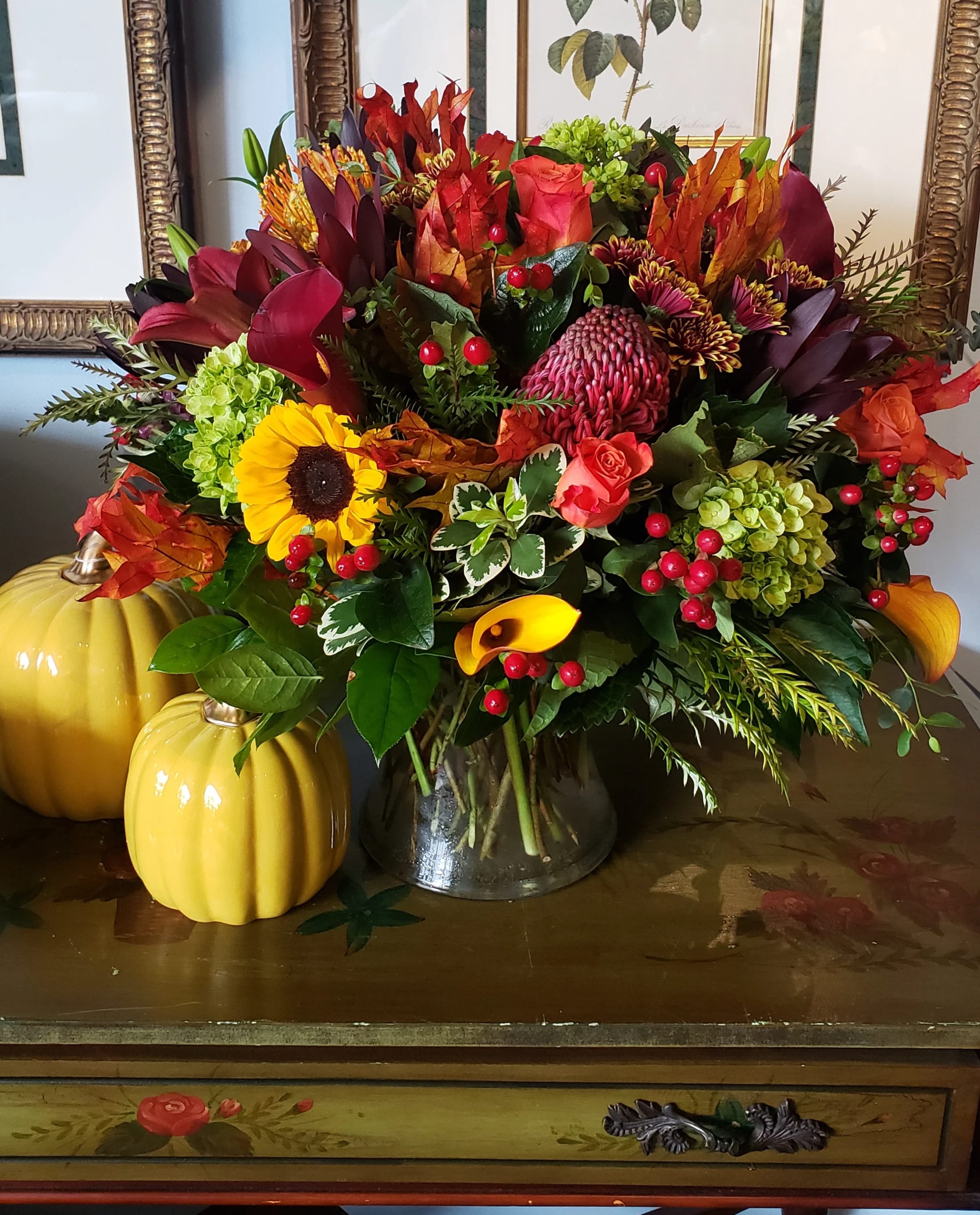 Fall in Love  -  An elegant gathering vase filled with seasonal bright flowers such as  sunflowers, protea ,orange crush roses, green hydrangea blooms, green dianthus red hypericum berries and other  garden flowers create a beautiful and bold autumn image.  **pot color may vary**