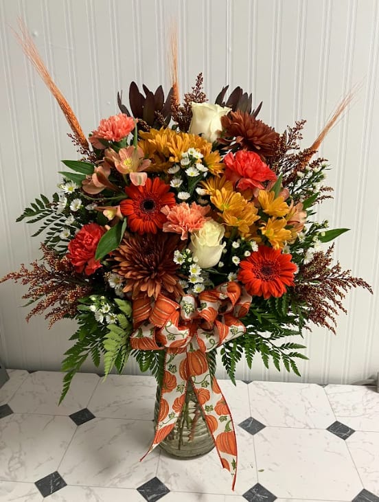 Pumpkin Pie  - Designed in a larger vase, this one-sided arrangement makes a warm seasonal statement. Featuring a festive pumpkin bow and an abundant mix of orange and bronze blooms, it’s rich in autumn color and charm. Perfect for a dining table, entryway, or sending as a generous fall gift, this piece captures the cozy spirit of the season—just like its namesake dessert. **Arrangement is one sided**