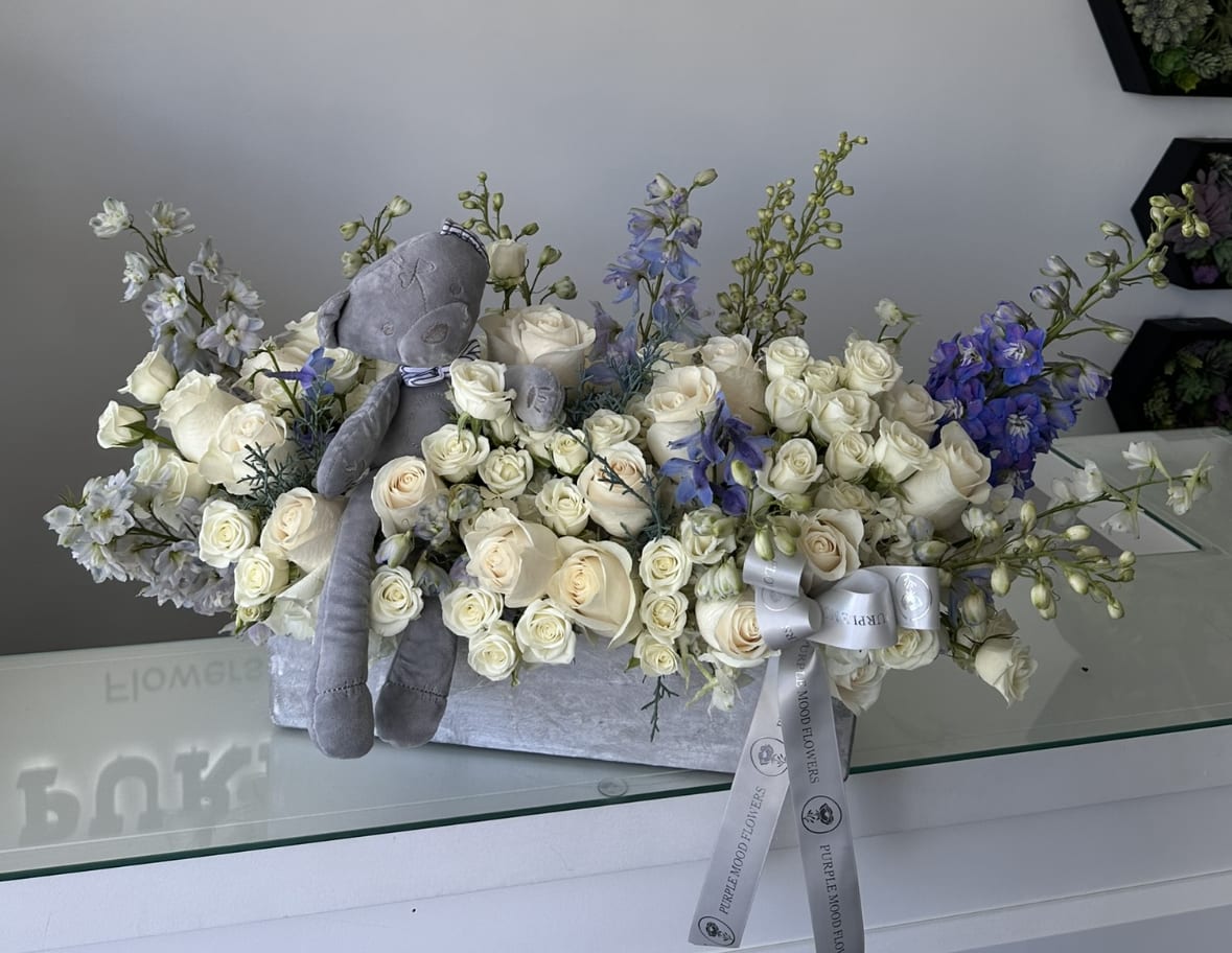 It's a Boy Vase It's a Boy Vase - Celebrate the joy of a new beginning with the It’s A Boy Vase. A graceful arrangement in soft whites and gentle blues, accented with a plush teddy bear and elegant ribbons, makes this design a thoughtful gift for welcoming a baby boy. Both charming and sophisticated, it’s perfect for baby showers, hospital deliveries, or home celebrations.  Key Features:     •    Styled in a modern elongated vase with soft blue and white tones     •    Includes a plush teddy bear keepsake     •    Finished with signature ribbon for a polished touch     •    A heartwarming gift for baby showers, hospital visits, or welcoming baby home
