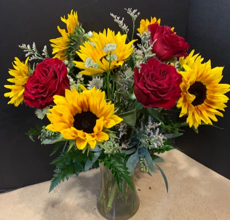 SUNSHINE AND ROSES  $110/160/210 - Beautiful vase of long stem premium red roses and smiling sunflowers in a colorful vase.   Each upgrade adds 6 additional stems of red roses.   Don't forget  to add a special finishing touch of chocolate, a fragrant candle, teddy bear or heart shaped Vintage brooch. 