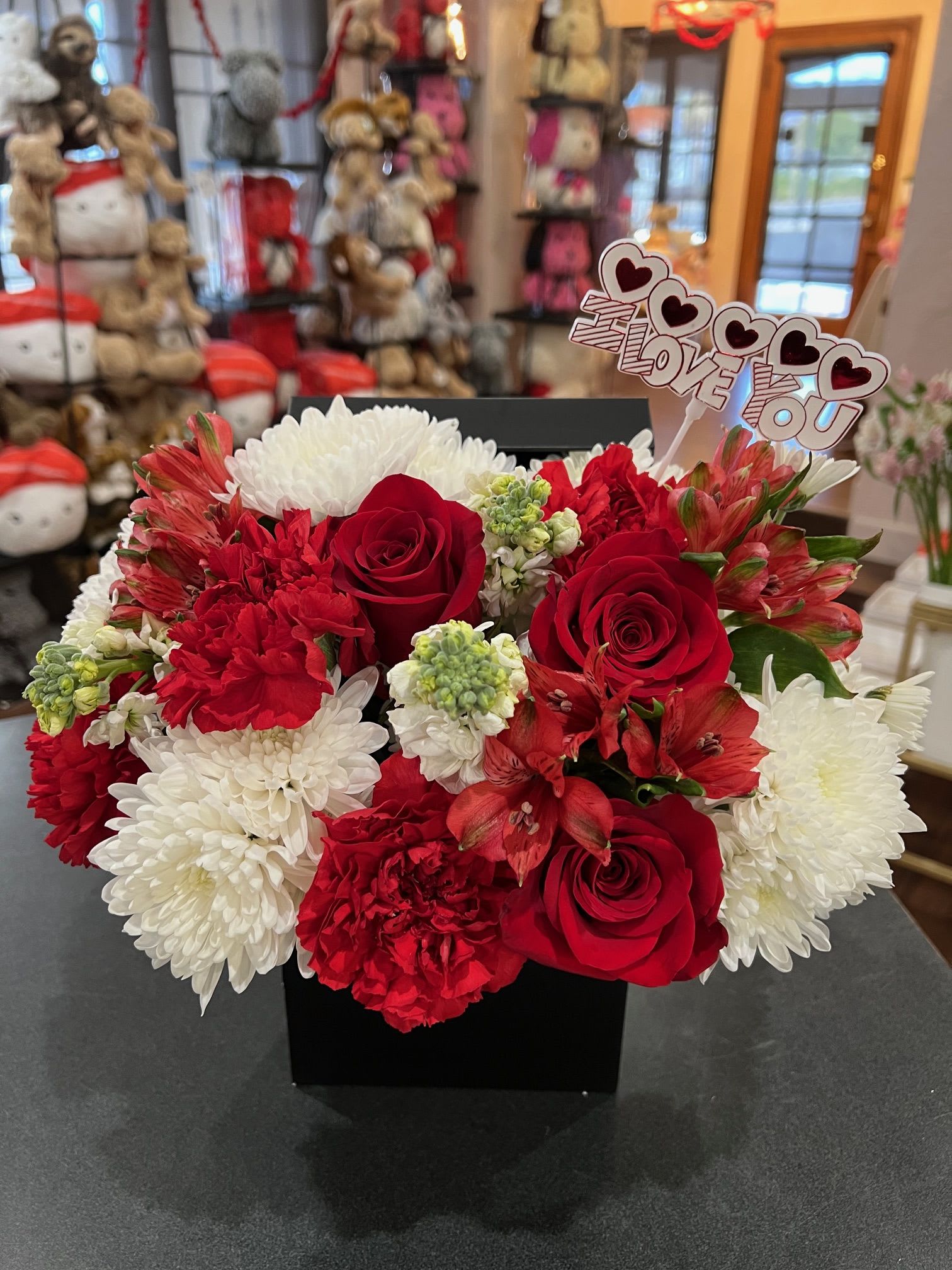 Red and White flowers in a black box - Red roses, red carnation, red alstromerias, white poms, and white stocks are arranged inside a black flower box.