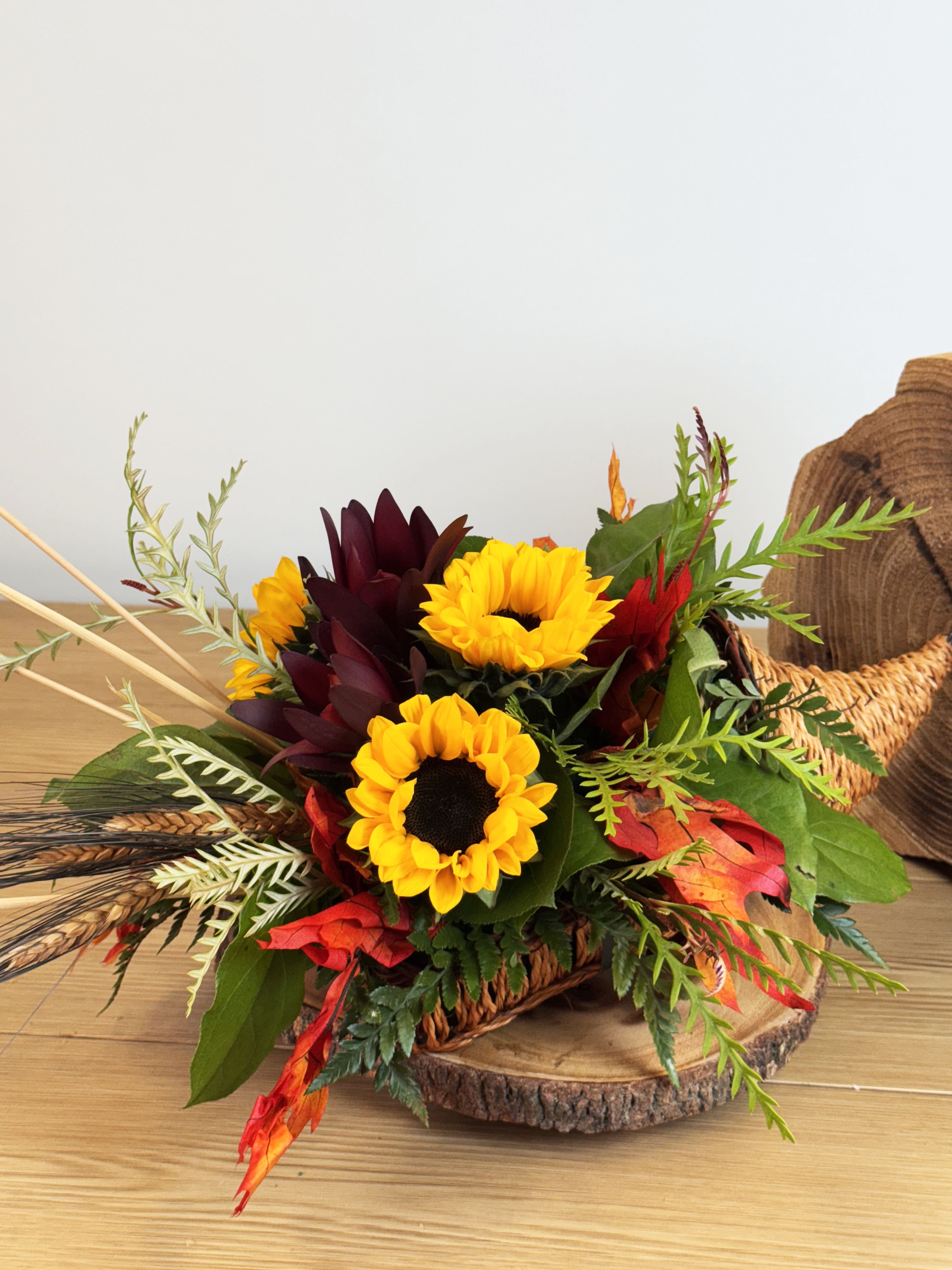 Thanksgiving Cornucopia Centerpiece (Available Nov. 17th-28th) - Celebrate the nostalgia of Thanksgiving with our charming Thanksgiving Cornucopia Arrangement. This simple yet elegant piece blends the transition of seasons, making it a delightful centerpiece for your holiday table.  Festive Christmas greens add a touch of wintery freshness.  Warm fall accents such as autumn leaves, mini pumpkins, and seasonal berries evoke the coziness of Thanksgiving.  Arranged in a classic cornucopia, symbolizing abundance and gratitude.  This timeless design bridges the joy of fall and the anticipation of the holiday season, creating a welcoming and nostalgic ambiance. Perfect for Thanksgiving gatherings, it brings both tradition and style to your celebration!