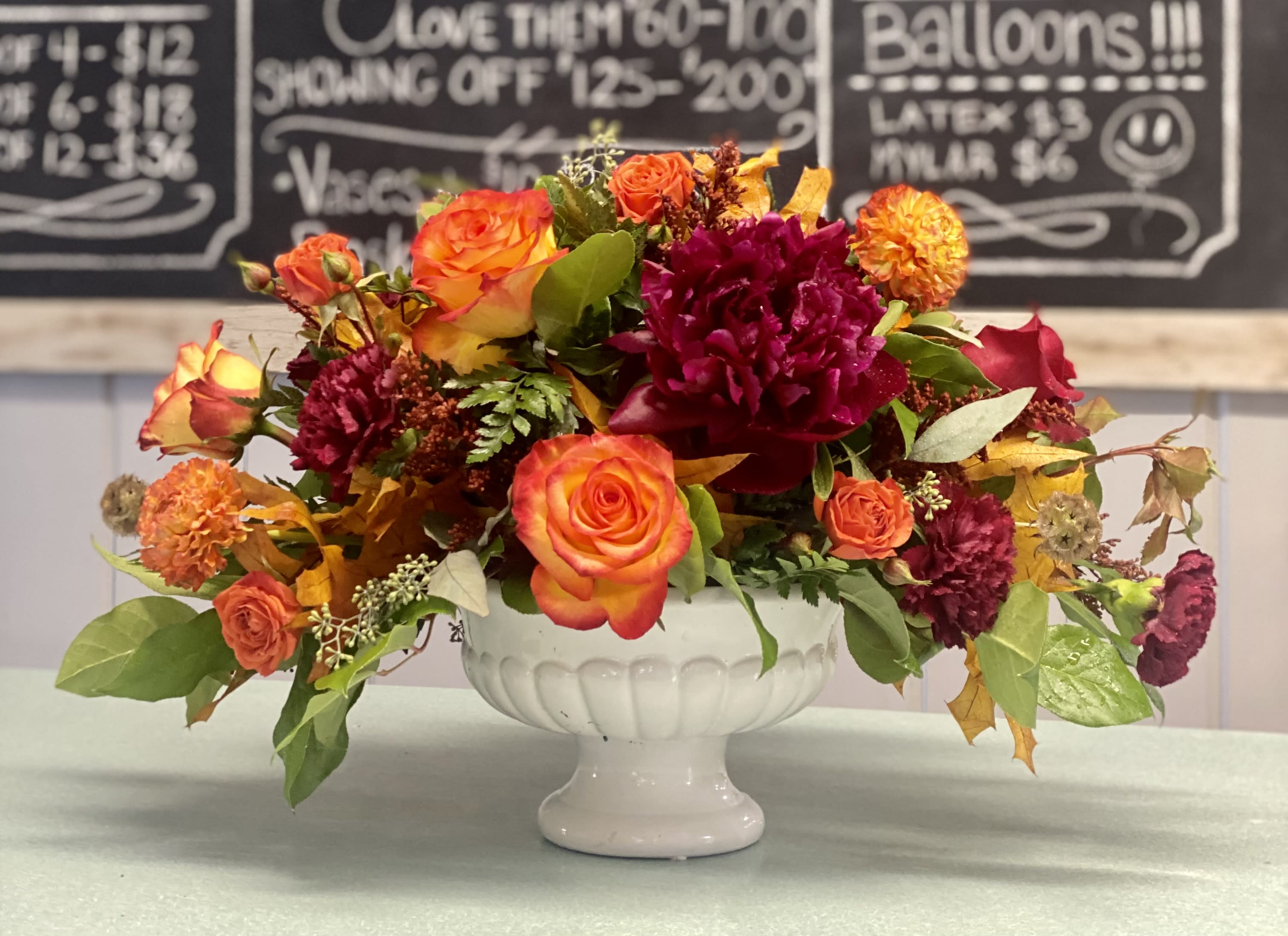 Give Thanks Give Thanks - High and magic roses, burgundy peonies, orange spray roses, burgundy carnations, orange straw flower with assorted greenery in a white pedestal bowl