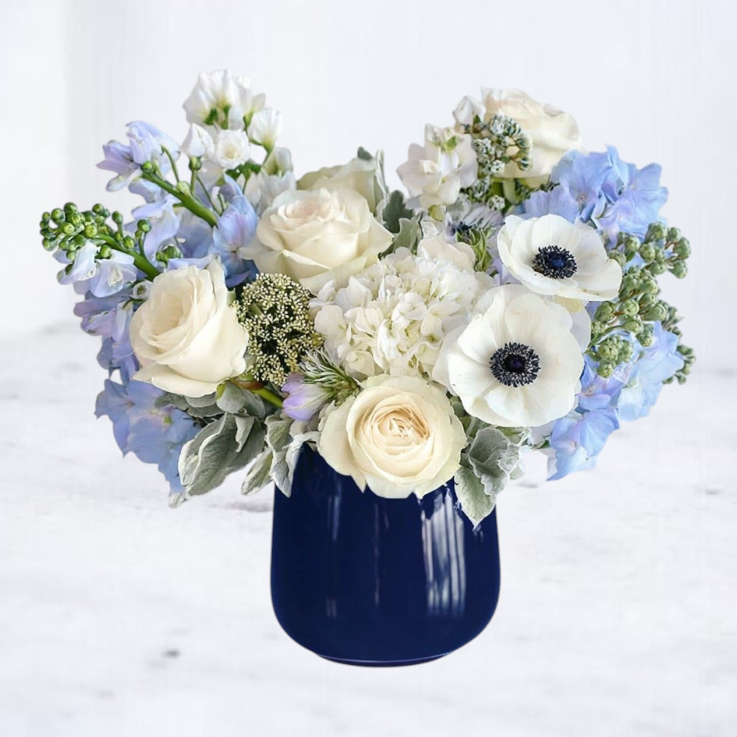 Ink & Ivory Ink & Ivory - Sympathy Flowers with White Roses & Anemones in a Navy Vase Graceful and grounding, Ink & Ivory offers a refined expression of remembrance. Featuring crisp white ranunculus, creamy roses, anemones, and textured foliage arranged in a modern navy vessel, this bouquet conveys comfort and quiet strength in a time of sorrow. Its neutral palette and contemporary styling make it a thoughtful choice for expressing condolences—whether sent to a memorial service, a grieving family’s home, or a place of worship. Sympathy flower delivery available for Houston, Magnolia, Montgomery, Willis, Porter, and surrounding areas.