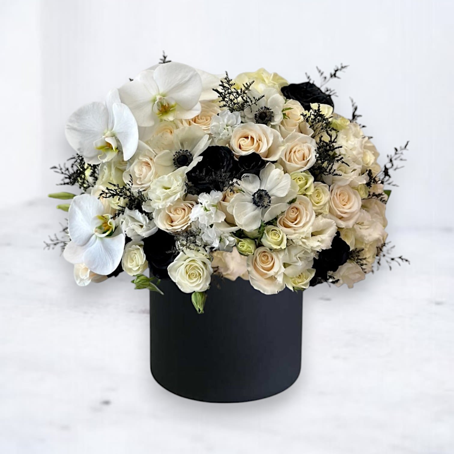 Obsidian Elegance Obsidian Elegance - Make a bold statement with the Obsidian Elegance, a striking floral arrangement that blends timeless beauty with modern sophistication. Featuring ivory and white spray roses, ethereal white orchids, dramatic black accents, and delicate lisianthus, this luxurious bouquet is artfully arranged in a sleek black vase. Perfect for special occasions, heartfelt condolences, or as a stunning centerpiece, the Obsidian Elegance captures the essence of refined style. Available for delivery in Houston and surrounding areas, this arrangement is an unforgettable gift or decor piece. Black and white luxury floral arrangement Elegant white rose and orchid bouquet Flower delivery in Houston Modern black and white floral design with anemones