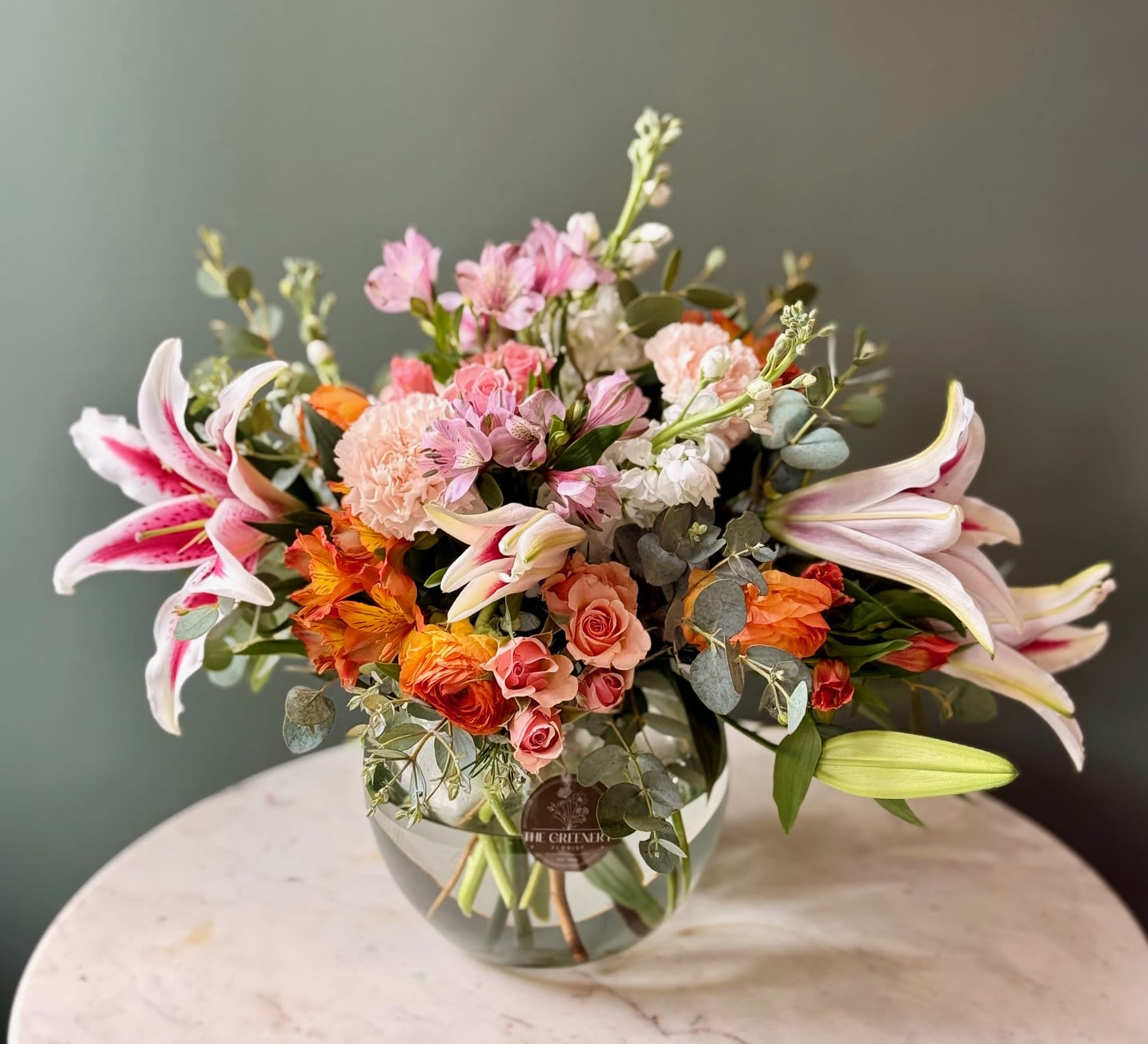 Southern Kiss - Soft and sweet, Southern Kiss features a dreamy mix of pink, peach, and white with pops of green. Flowers include lilies, spray roses, alstro, ranunculus, stock, and greenery. Arrangement is delivered in an 8&quot; H clear bowl. 