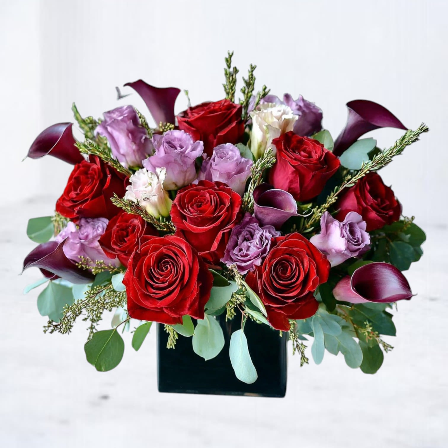 Crimson Amour Crimson Amour - Intense, romantic, and unforgettable — the Crimson Amour Bouquet features velvety red roses paired with exotic plum calla lilies and soft lavender blooms. Designed in a sleek black cube vase, this modern arrangement radiates luxury and sophistication. Perfect for anniversaries, birthdays, or simply expressing heartfelt love, this bouquet is a striking choice for anyone who appreciates bold beauty. Available for same-day flower delivery in Magnolia, The Woodlands, Spring, and Montgomery, TX, ensuring your message of love arrives right on time.