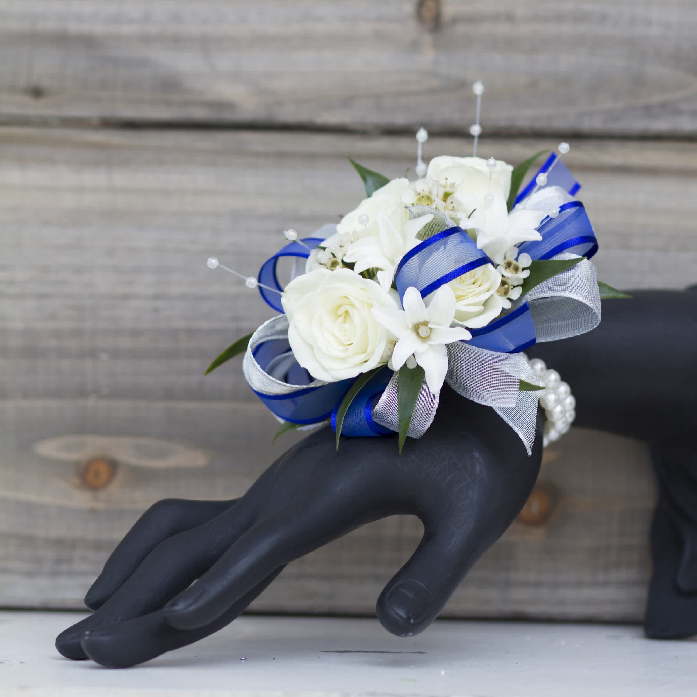 Milan - Classy white and bright blue blooms and greenery are showcased on a black, silver or white wristband.  The best blooms in this color will be selected by our designers. Upgrade to Deluxe to add a boutonniere!   Pick up dates for homecoming are Saturday, September 27th and Saturday, October 4th. Please call if you need to order this for a different event.